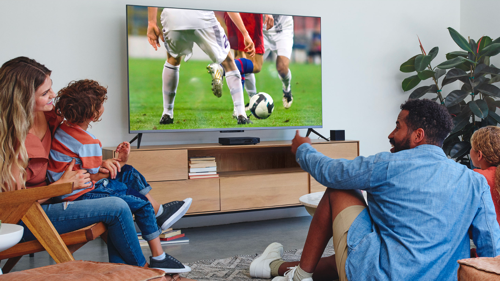 a group of people watching a soccer game on a tv controlled by a fire tv cube in a gray living room