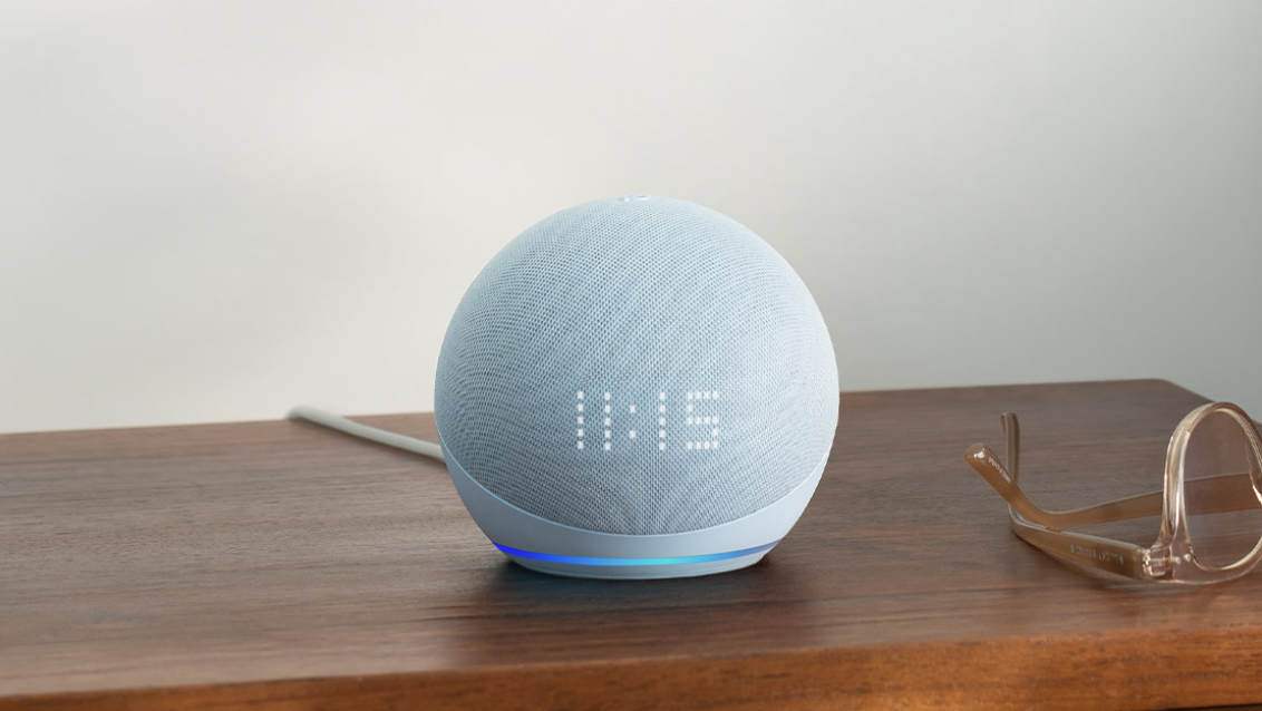 The 5th generation Echo Dot with clock resting on a table next to a pair of glasses