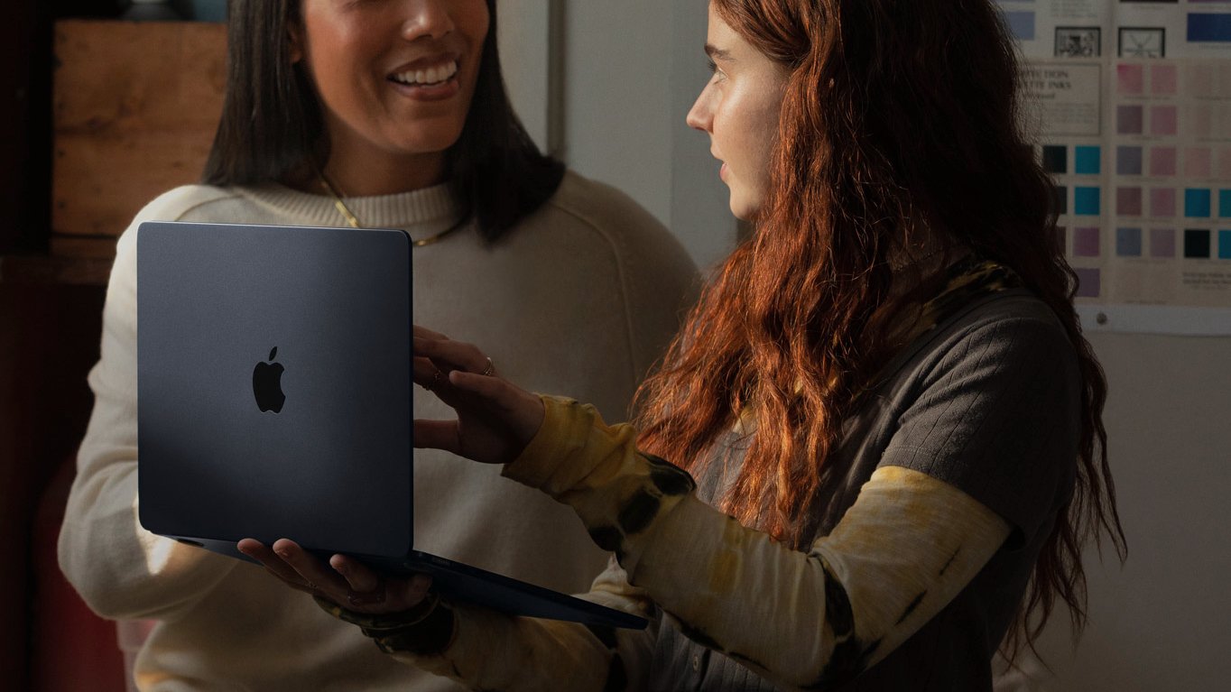 woman holding apple m1 macbook air and talking with another woman