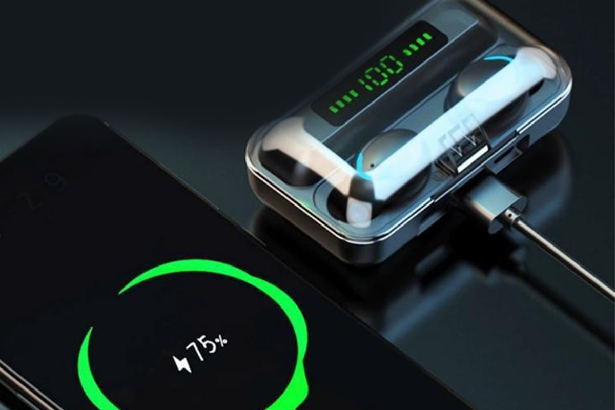 The Ninja Dragon wireless earbuds shown in their case next to a phone that's charging. 
