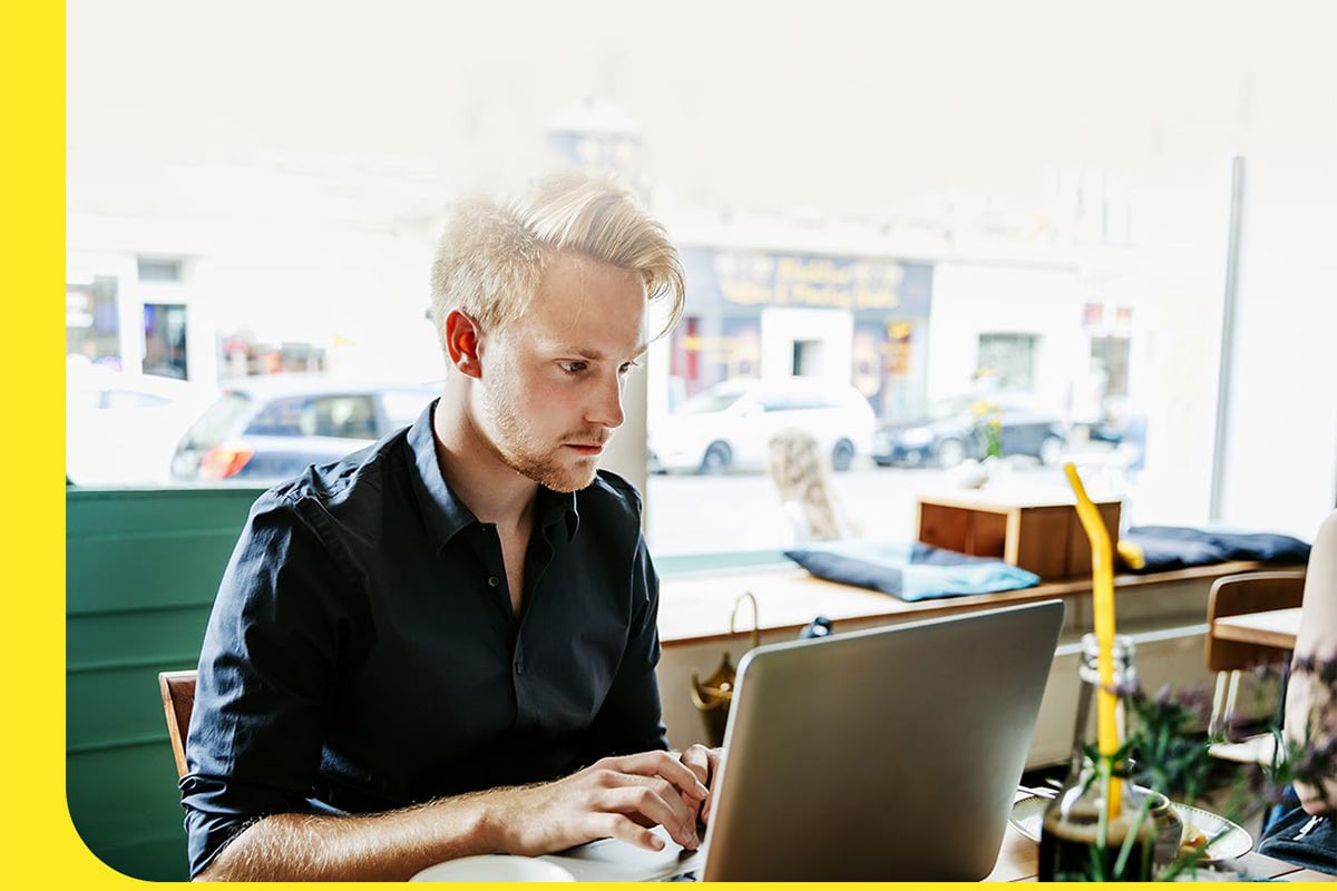 A man focusing intently on something pulled up on his computer while sitting inside a cafe.