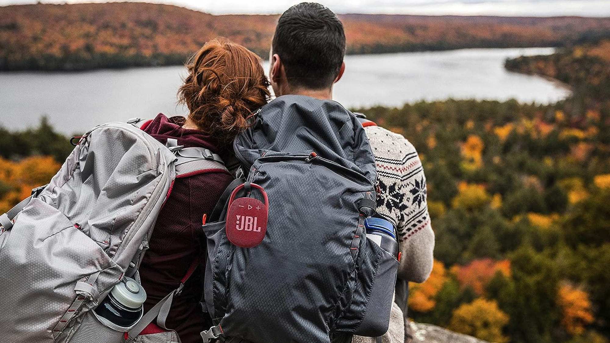 two campers sitting with their backs towards the camera and a JBL speaker on their bookbag