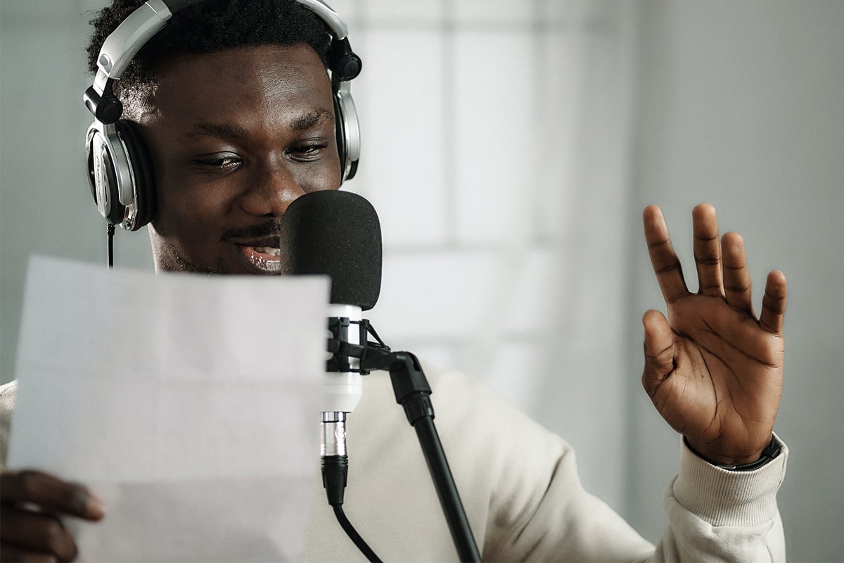 Someone holding up a sheet of paper while wearing headphones and voicing over script.