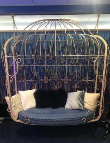 Gold hanging cage surrounding a blue bench.