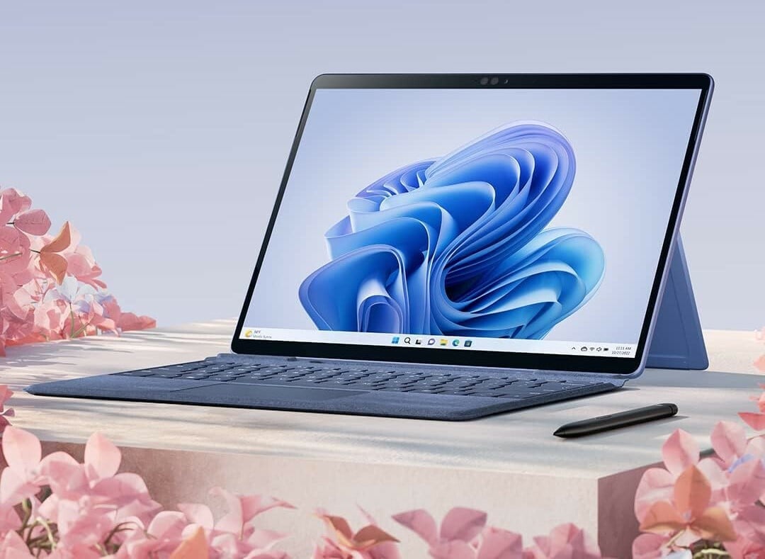 a microsoft surface pro 9 on a table with pink flowers in the foreground