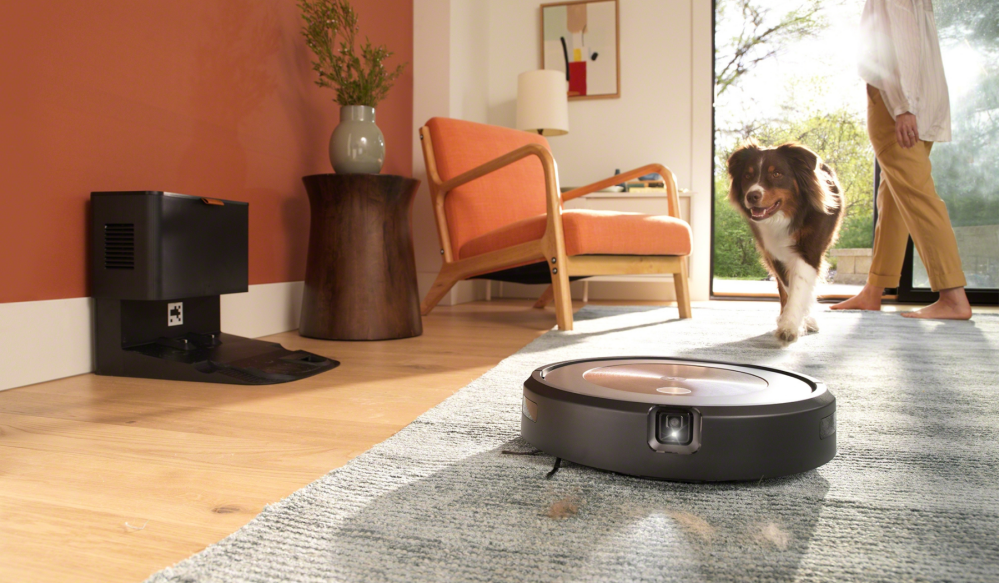 Roomba with headlight cleaning carpet with dog and person's feet in background