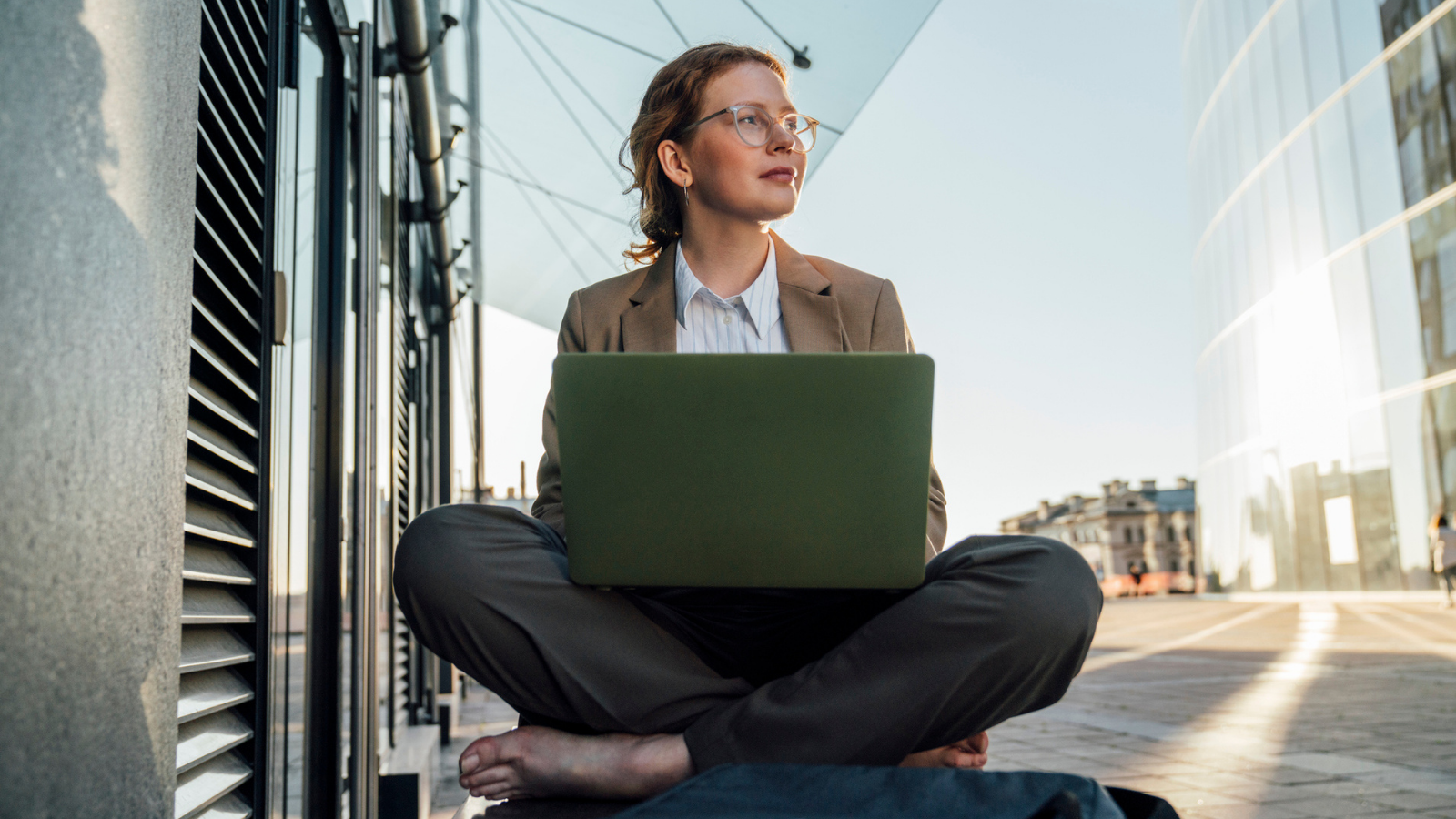 Thoughtful businesswoman sitting cross-legged with laptop on bench