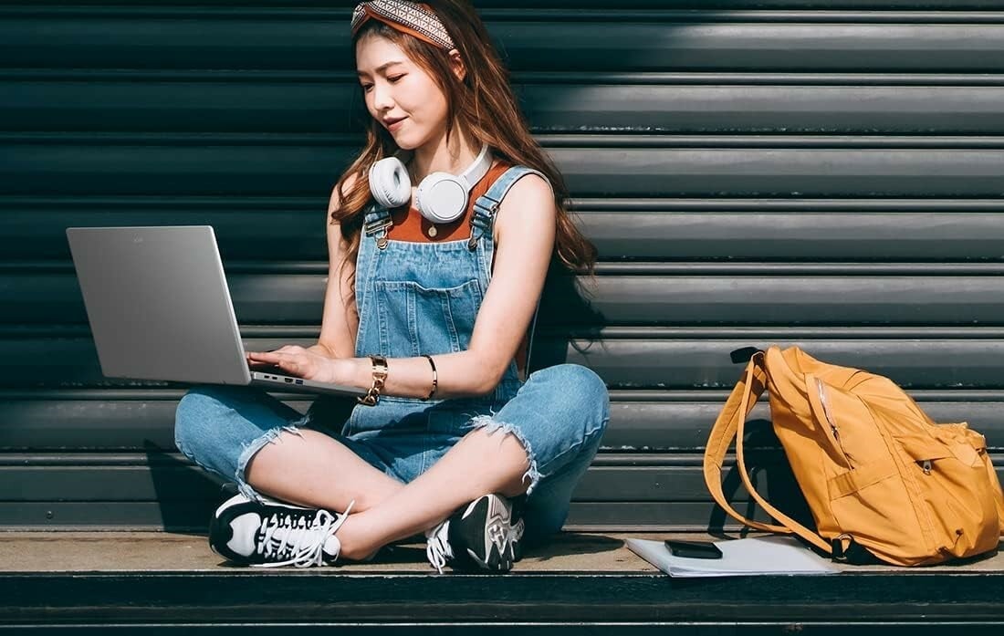 a woman sits on the ground with an acer laptop in her lap while she's typing