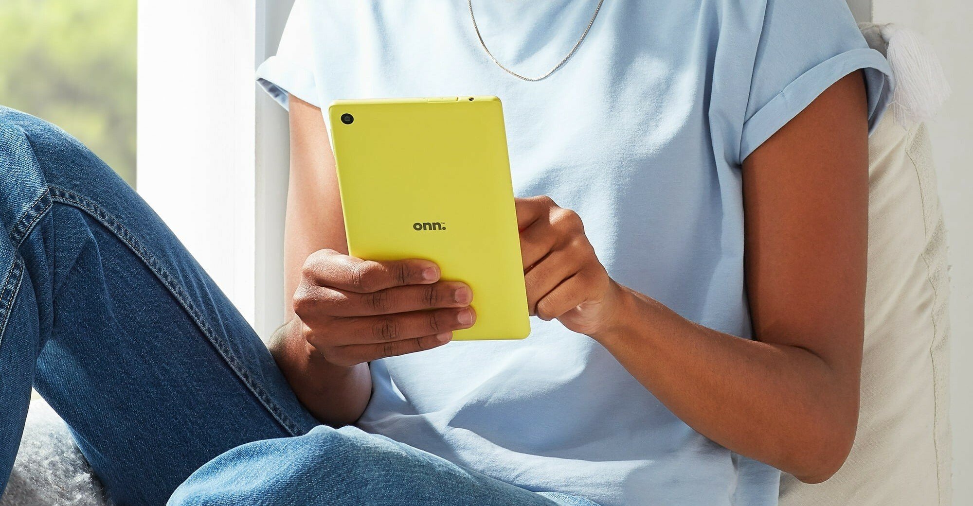 a yellow onn. tablet held by someone wearing a blue shirt and jeans while sitting next to a window