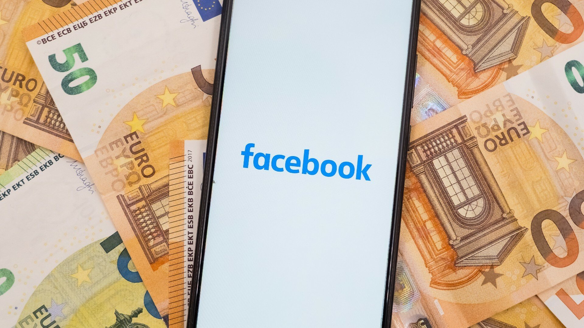 Facebook logo on a smartphone sitting on a pile of money