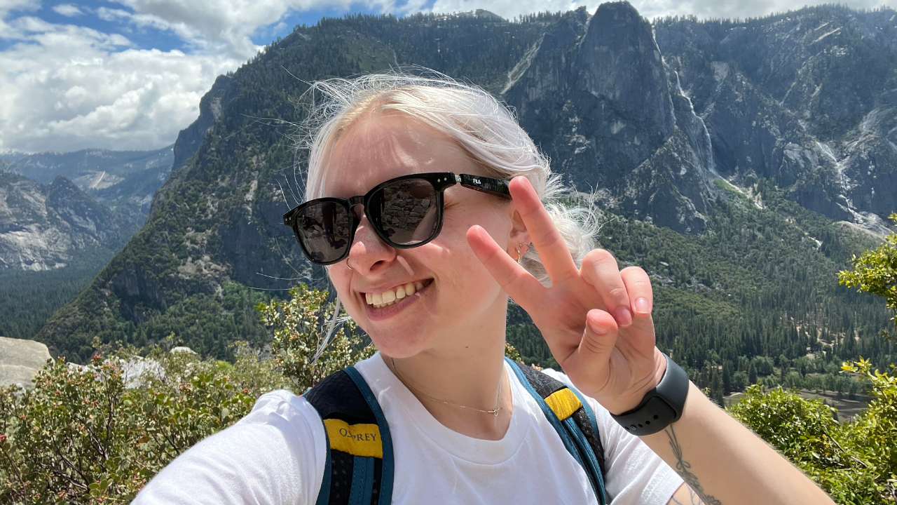 woman wearing sunglasses holding up a peace sign with mountains in the background