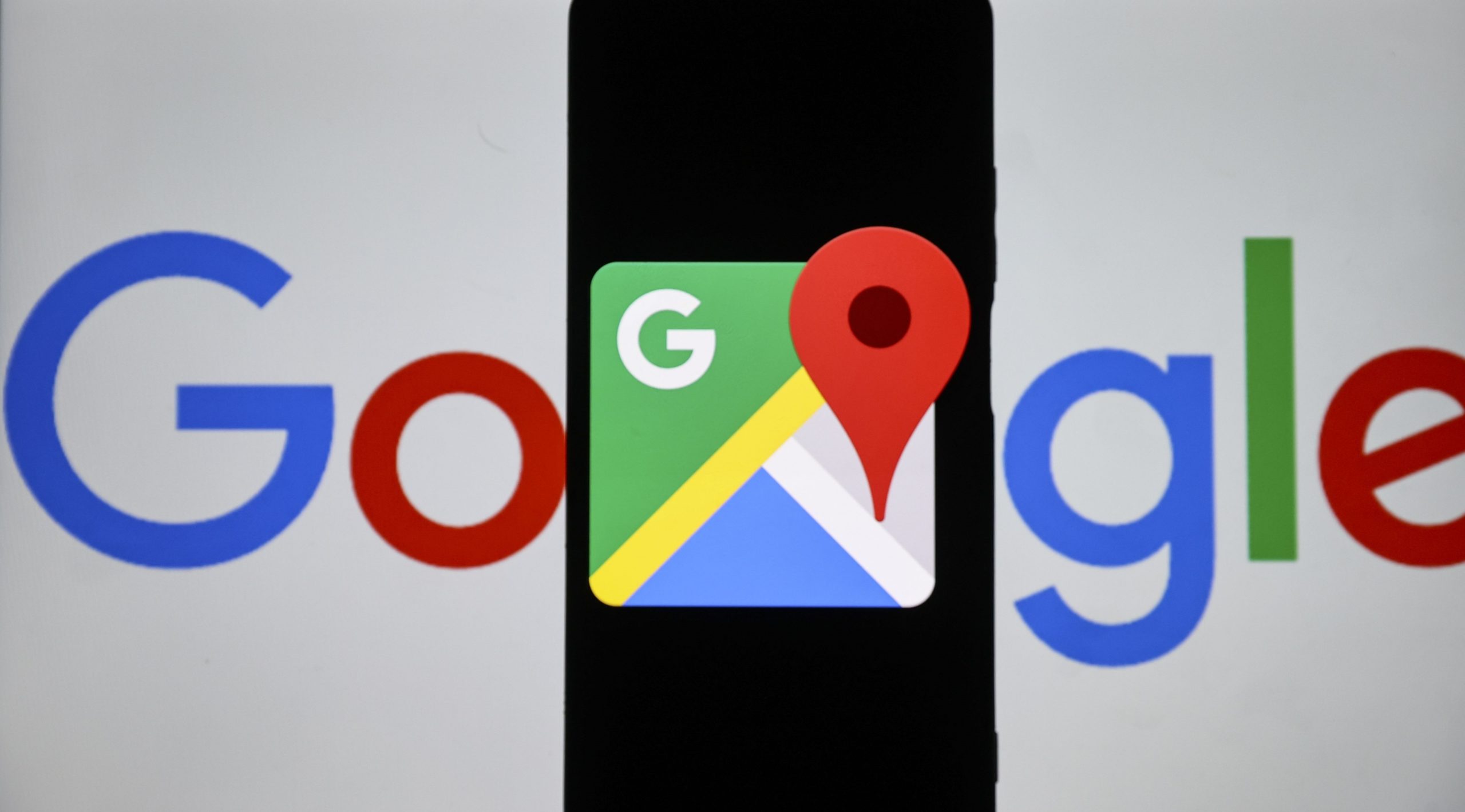 Google Maps logo displayed on a phone held in front of a Google logo.