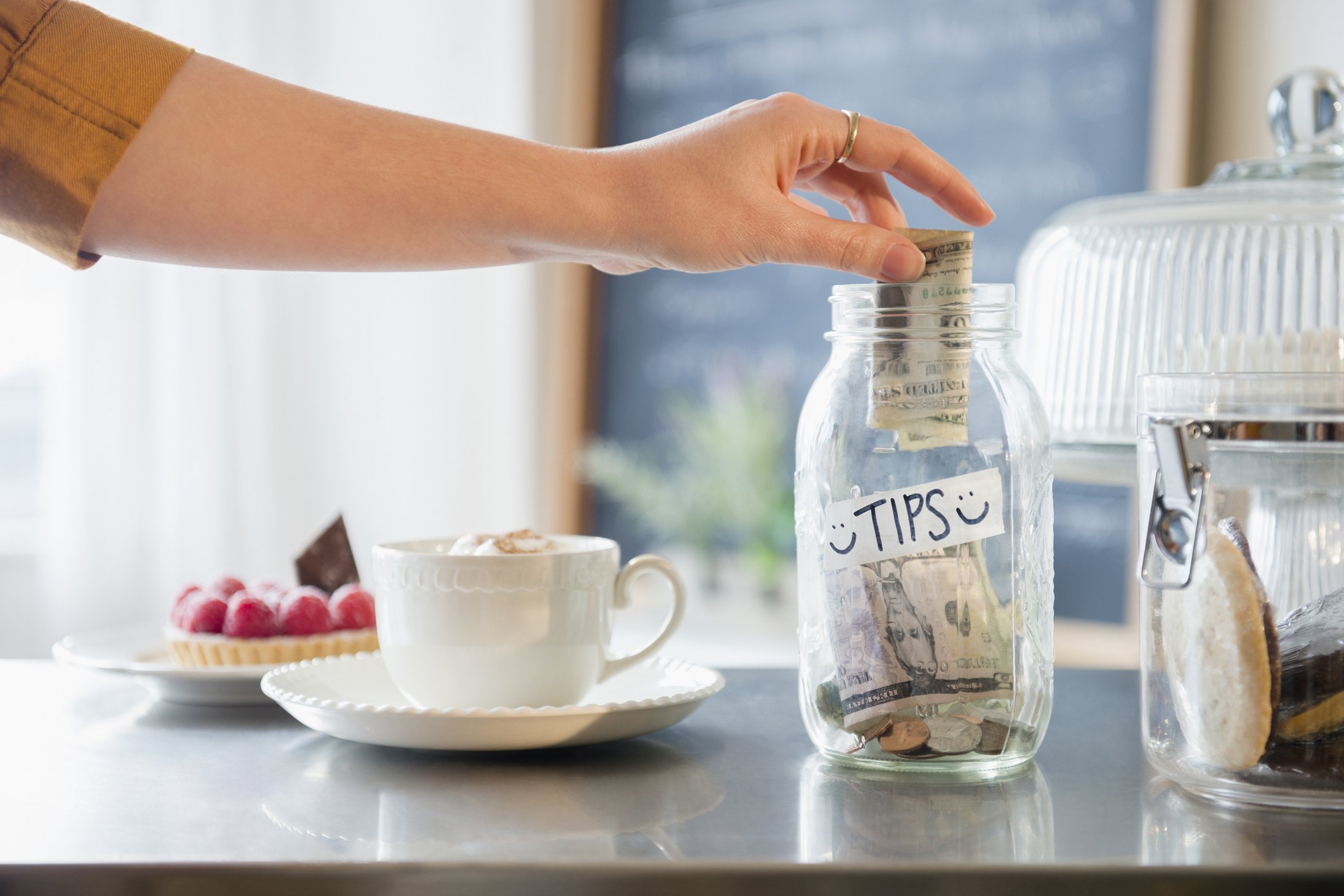 person's hand putting money in a tip jar