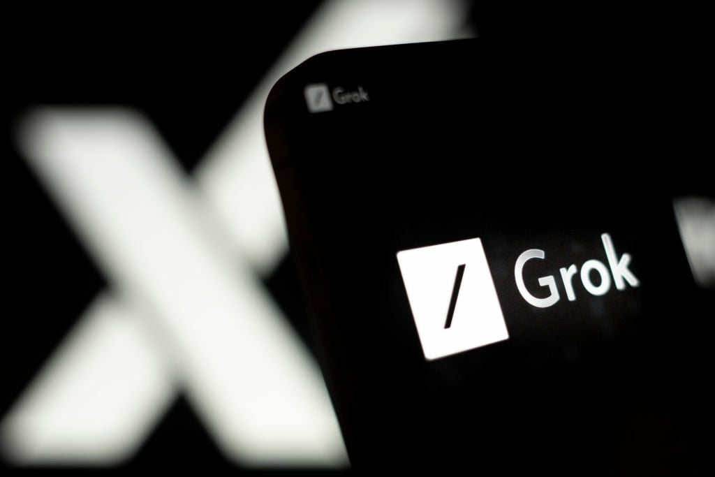The xAI Grok logo on a mobile phone in front of a screen displaying the X logo.
