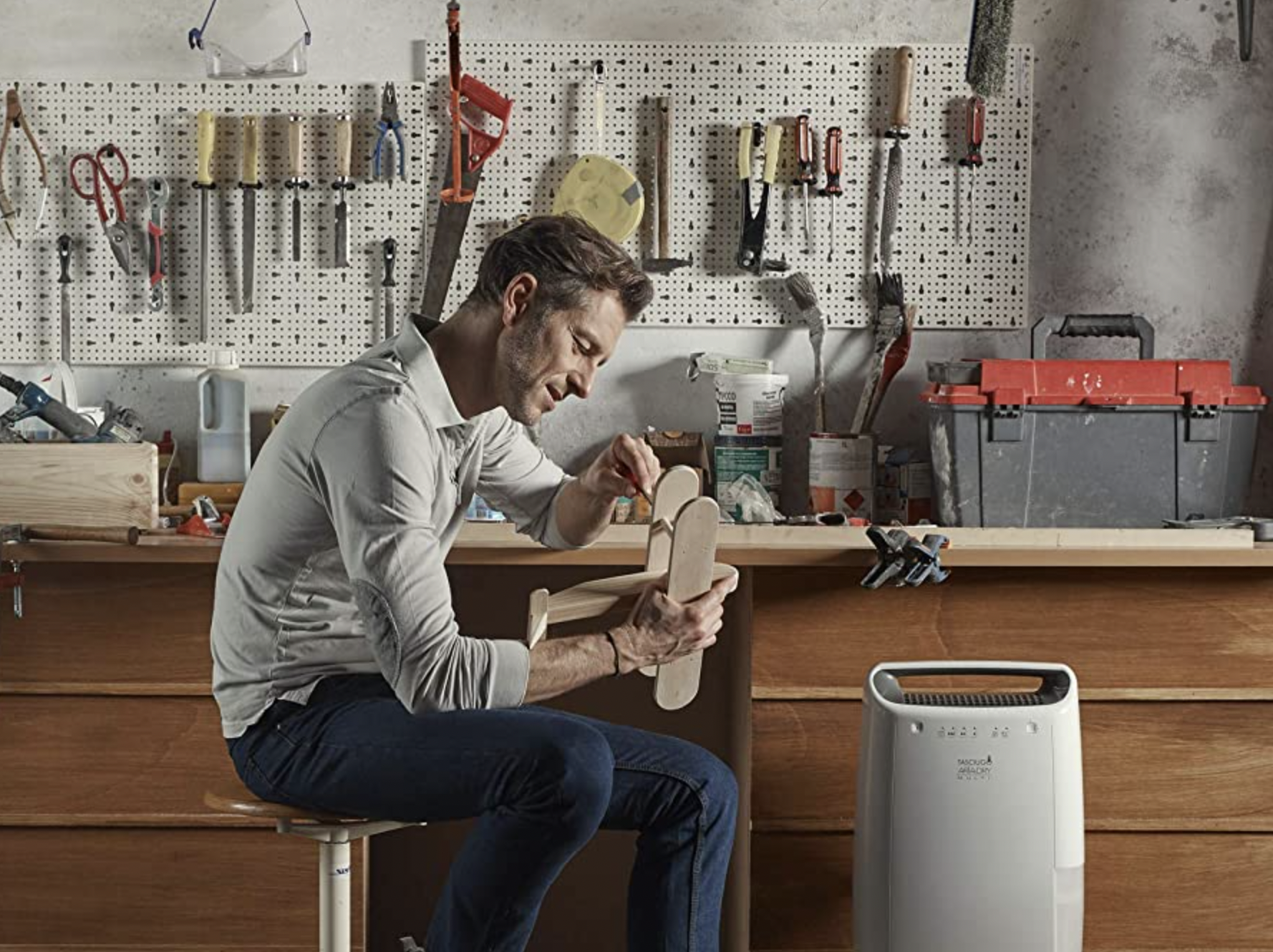 Man in a workshop crafting a toy, next to a dehumidifier