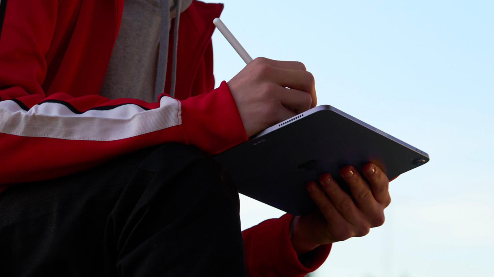 a close-up of a person writing on an apple ipad air with an apple pencil outside