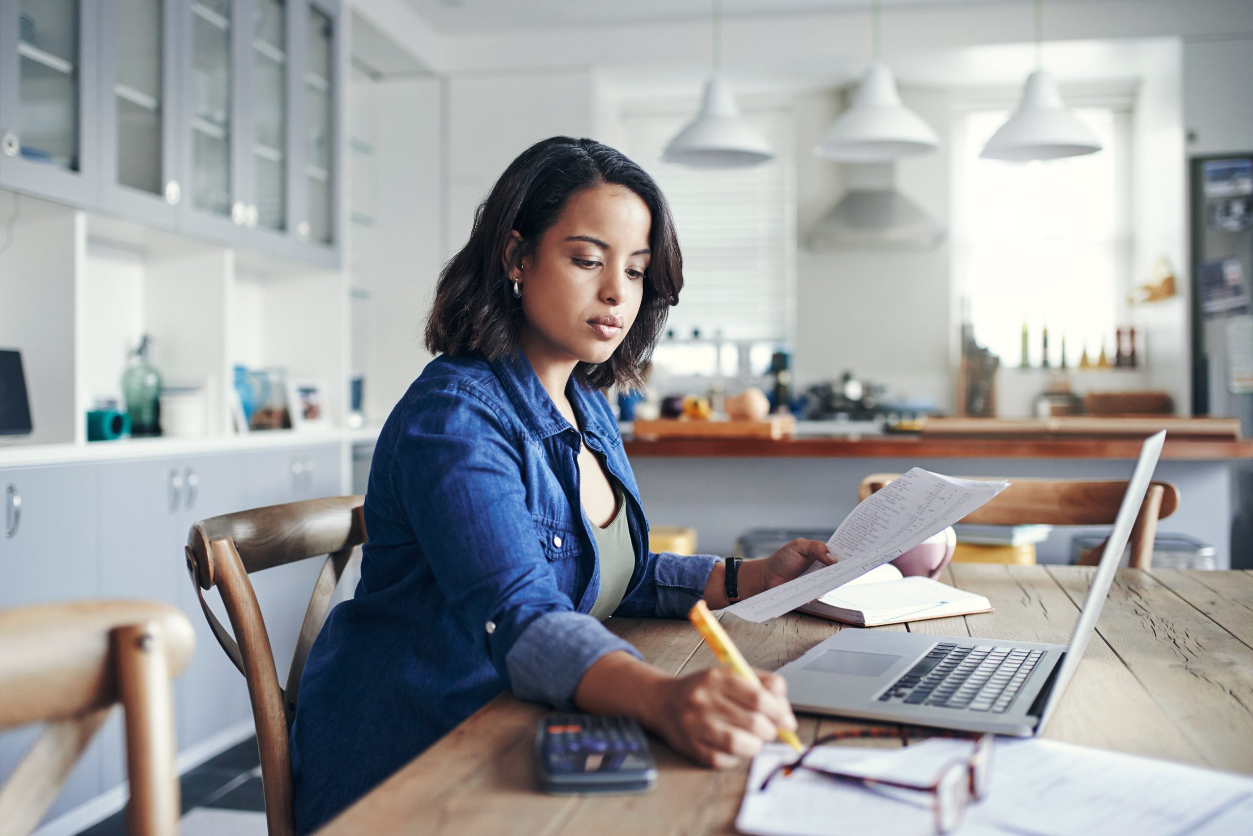 woman writing and using a laptop at home