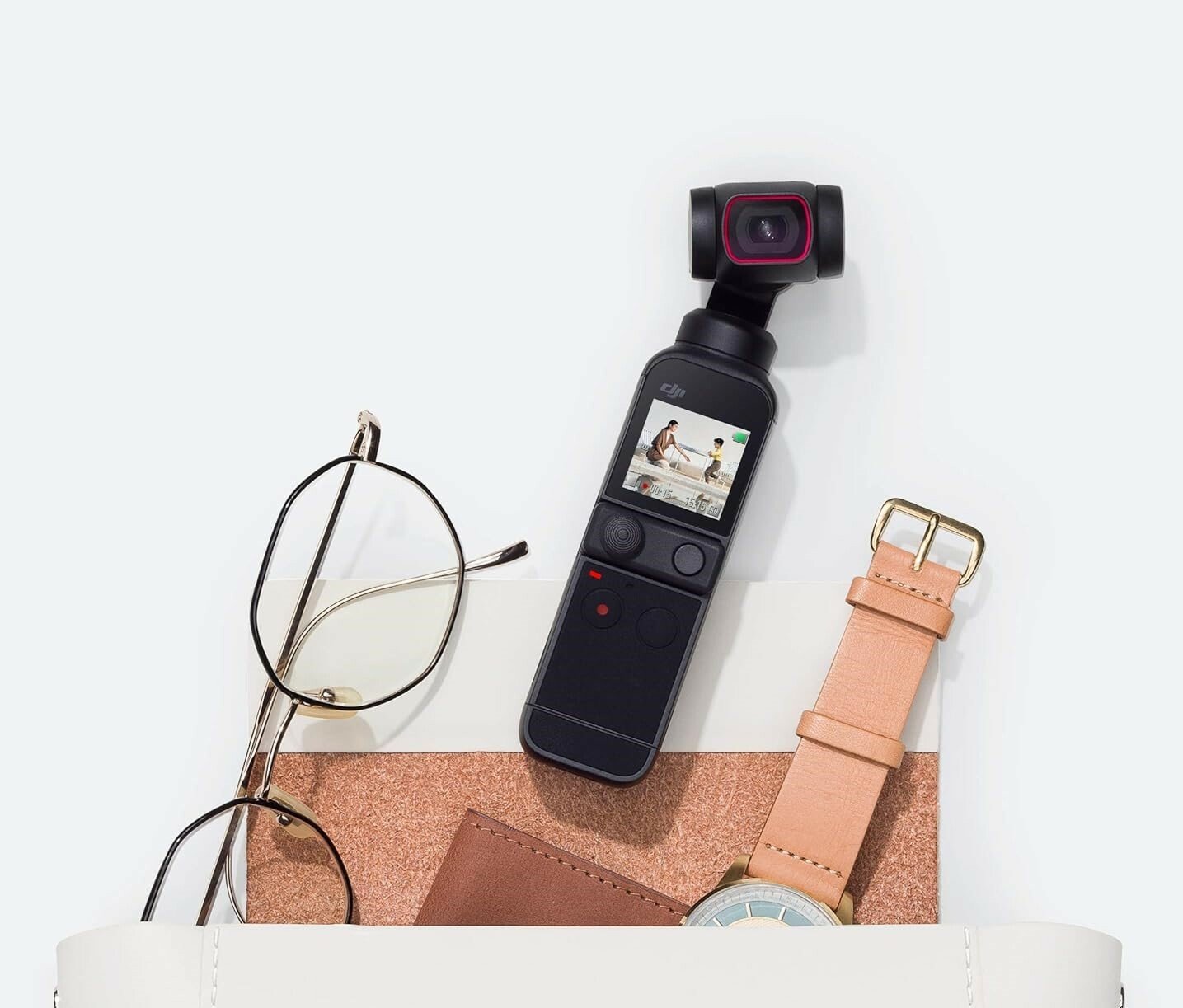 a DJI pocket 2 camera spills out of a bag, laying next to a pair of glasses, a watch, and a notebook.
