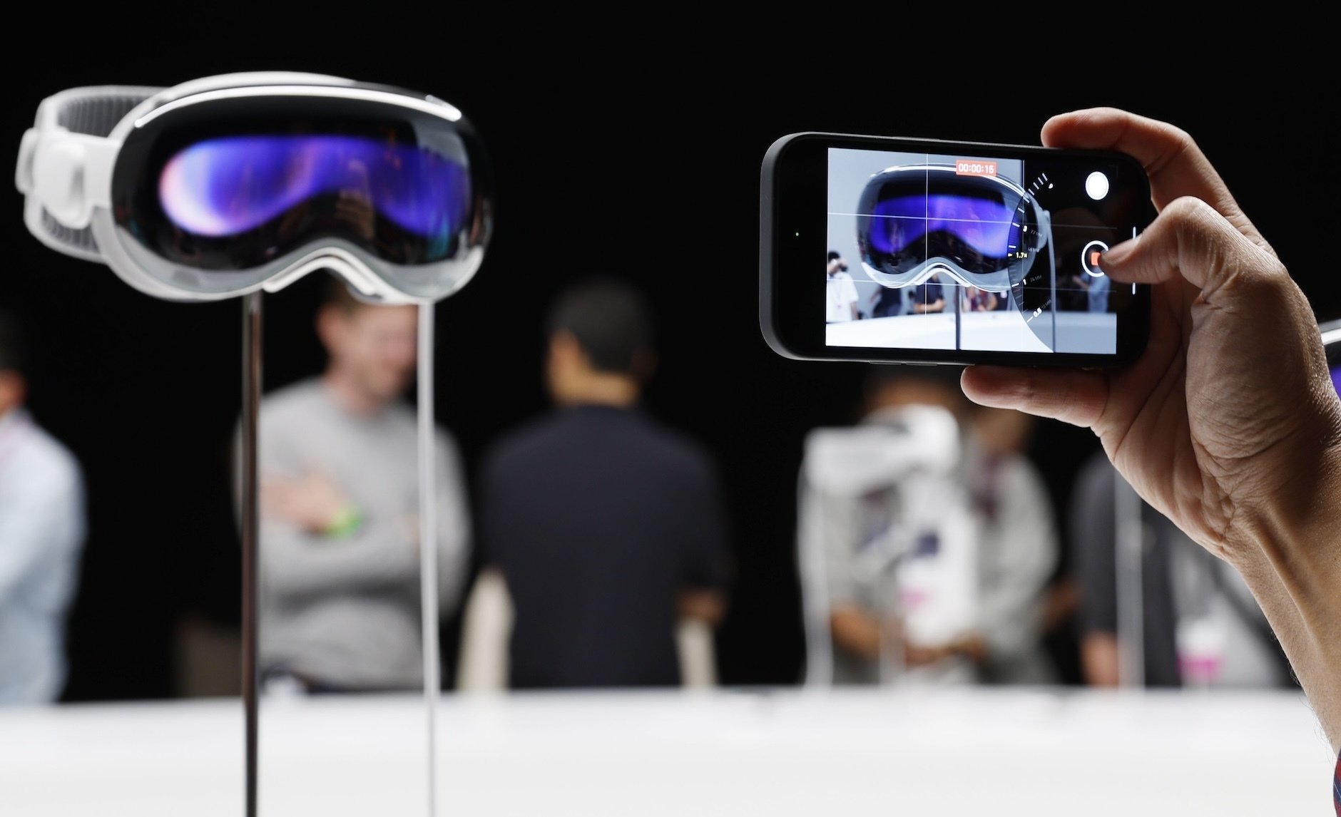 Apple's Vision Pro headset, and a man's hand taking a photo of it on an iPhone. 