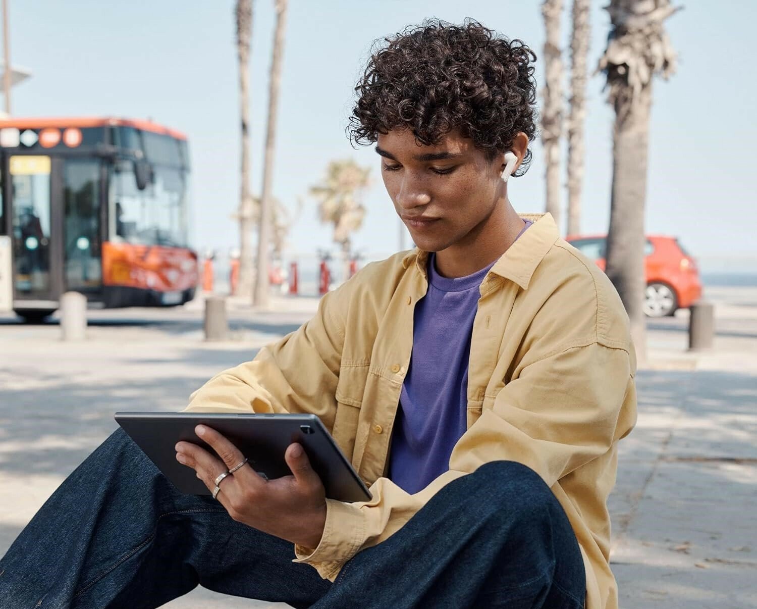 Boy sits outside using a tablet and JBL Tune 230 earbuds 