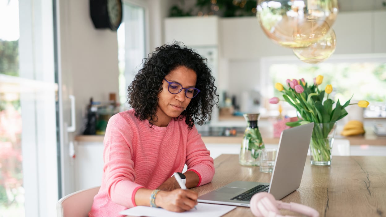 Person writing next to laptop