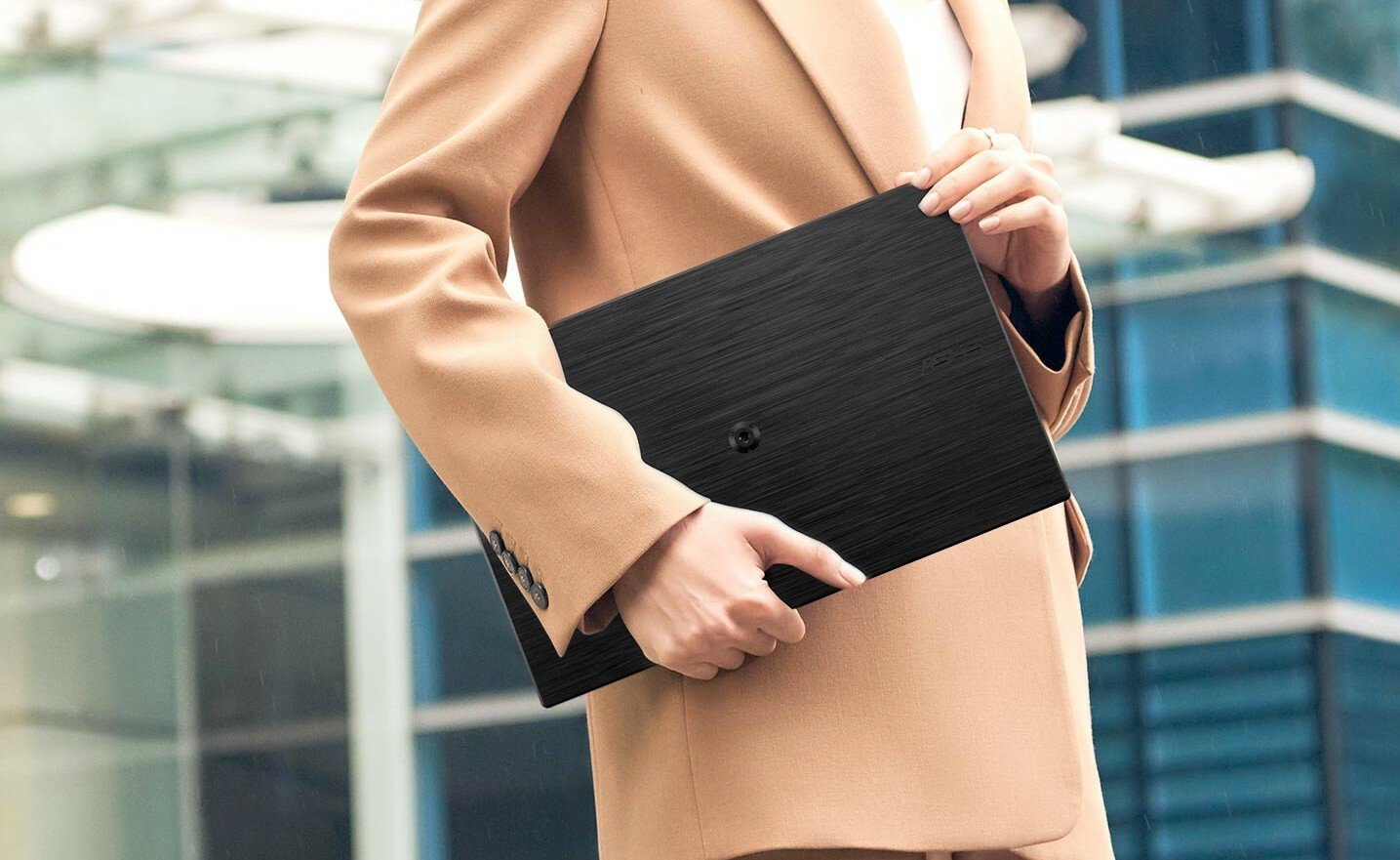 a person wearing a khaki colored suit holds the asus zensceen portable monitor while standing outside of a building