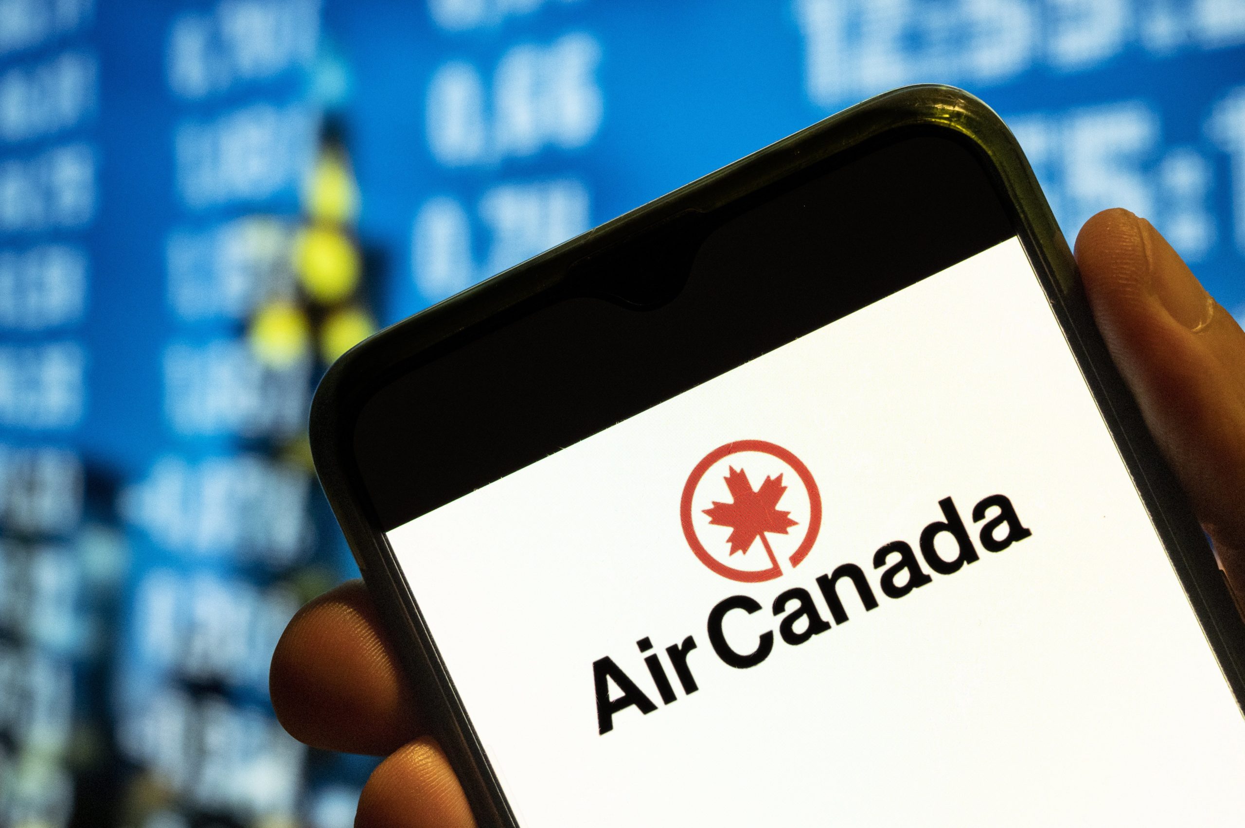 A phone displaying the Air Canada logo in front of a blue departures screen.