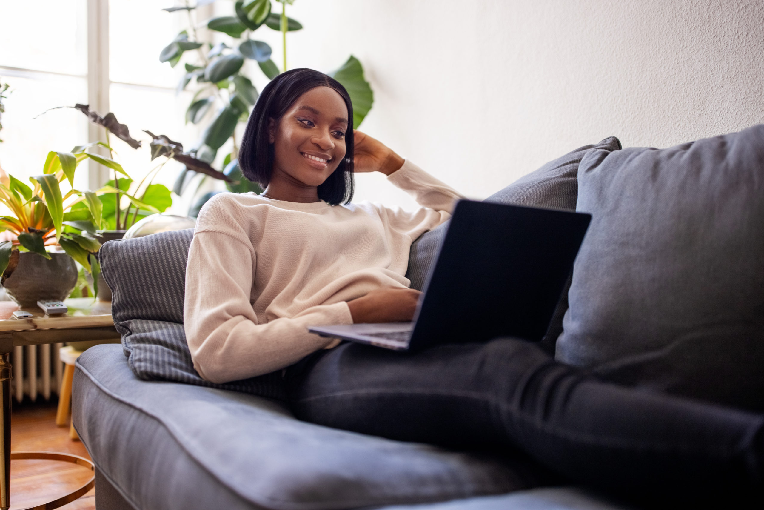 Woman on couch smiling at laptop.