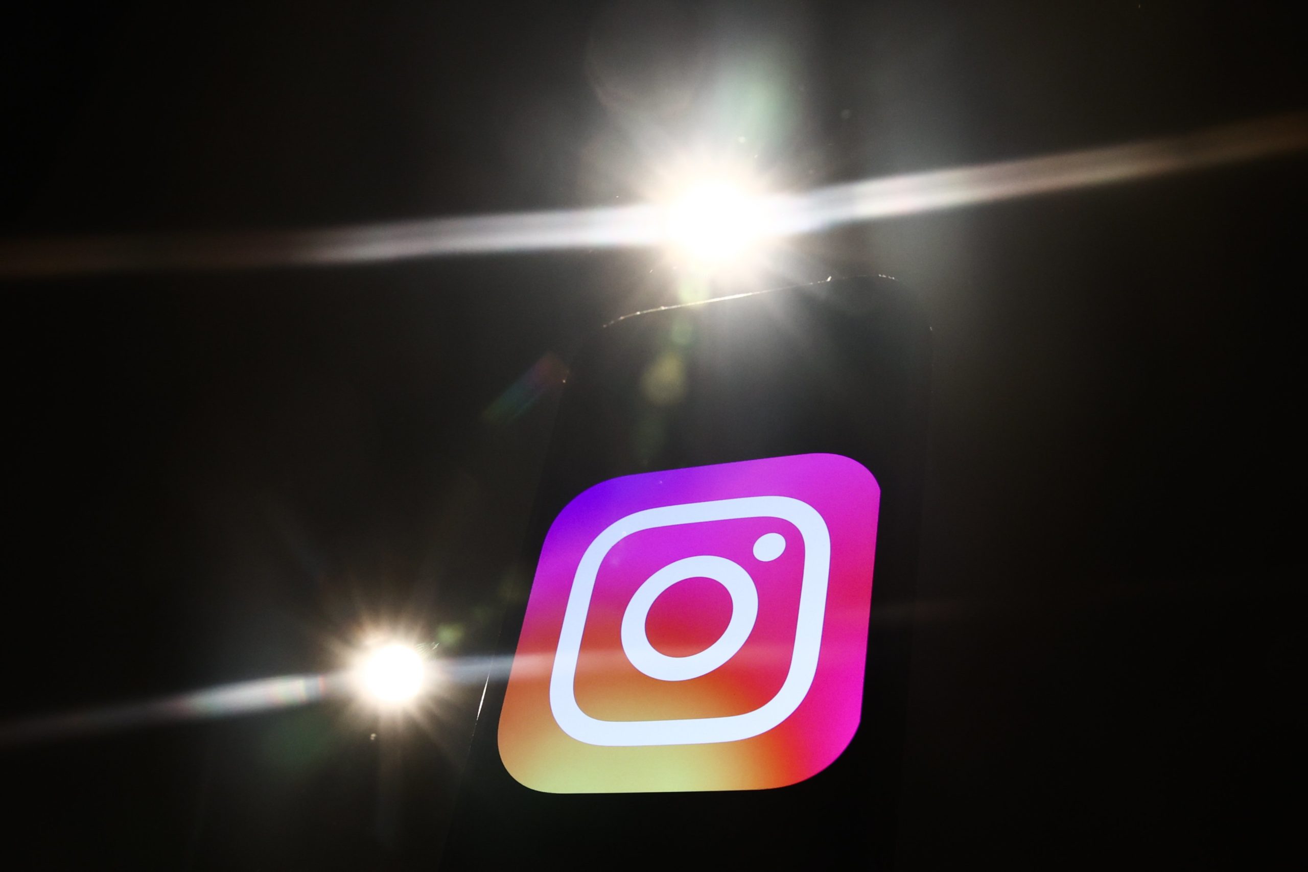 The Instagram logo on a black background. Bright camera flashes light up around it.