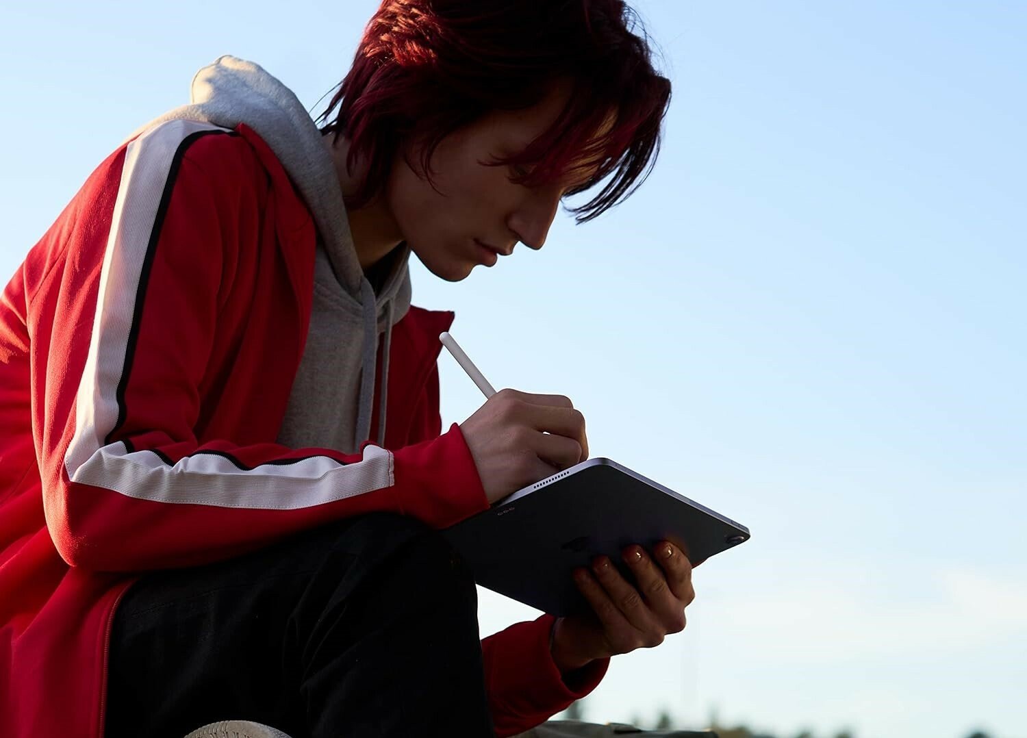a person sits cross-legged outside while using an apple iPad air tablet with an apple pencil