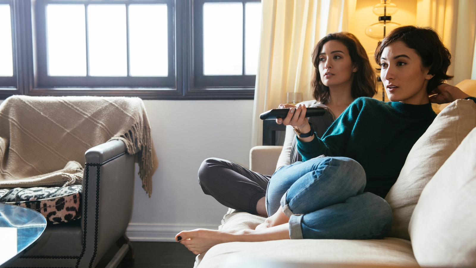 two women sitting on couch watching TV