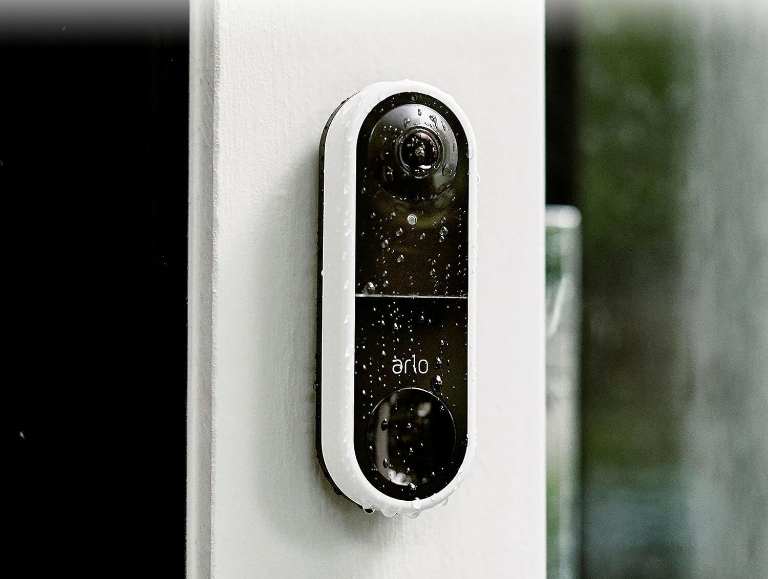 the arlo essential wired video doorbell on the site of a house while its raining