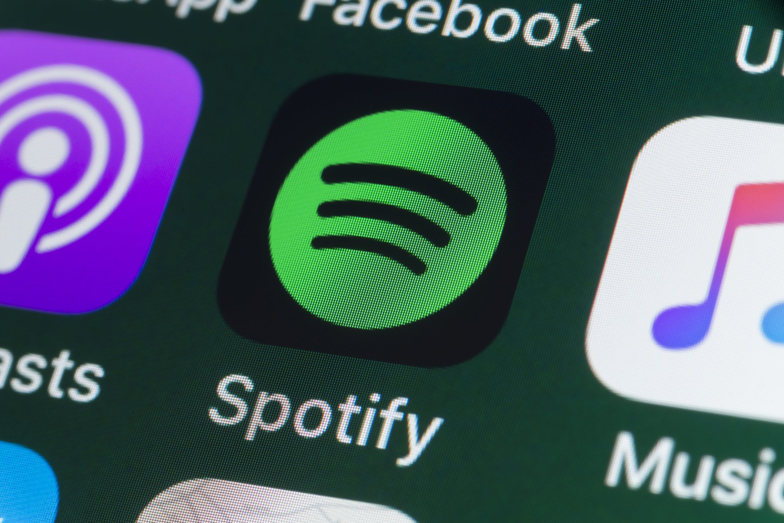 The buttons of the music streaming app Spotify, surrounded by Podcasts, Apple Music, Facebook and other apps on the screen of an iPhone.