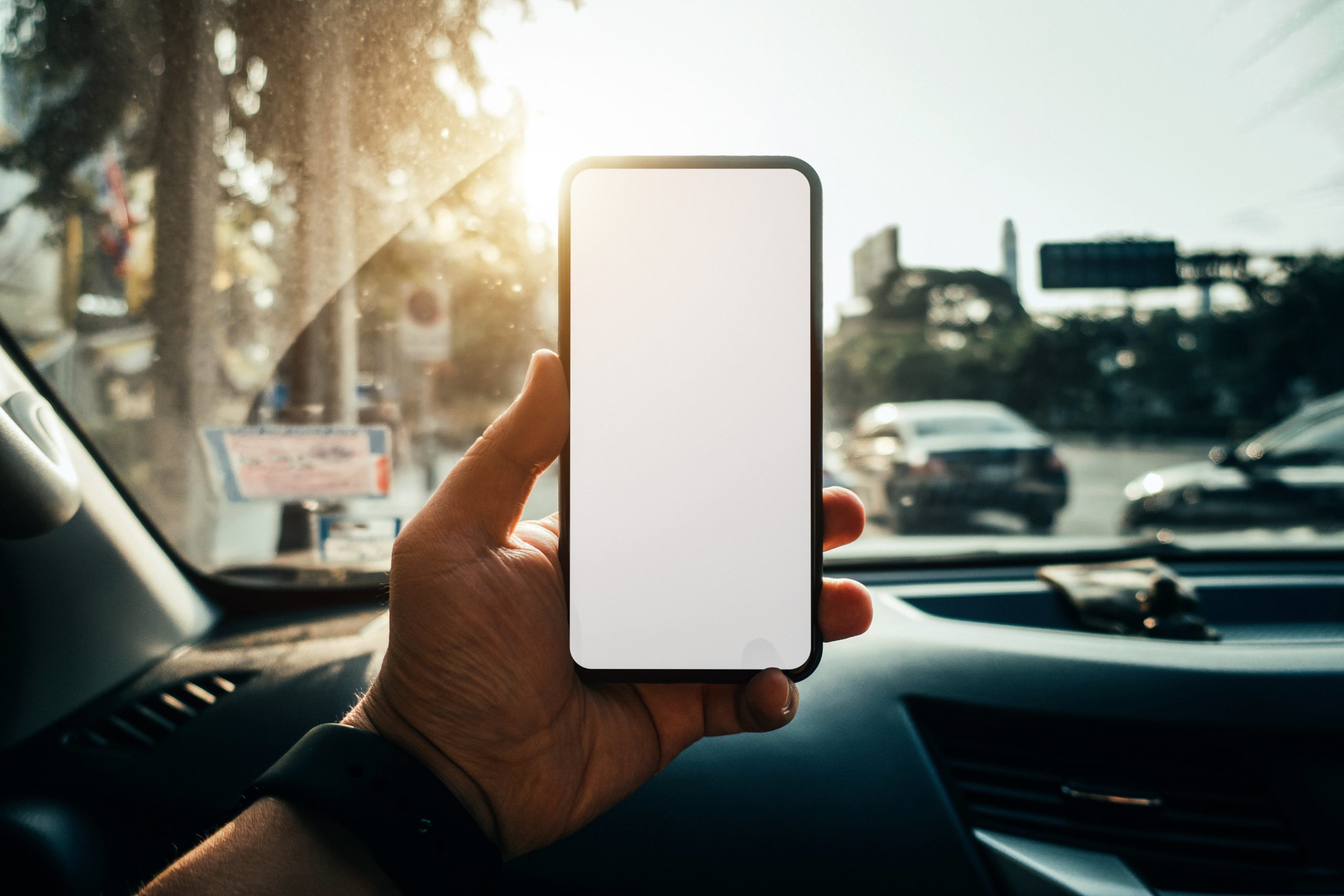 A hand holding an iPhone over a car dashboard.
