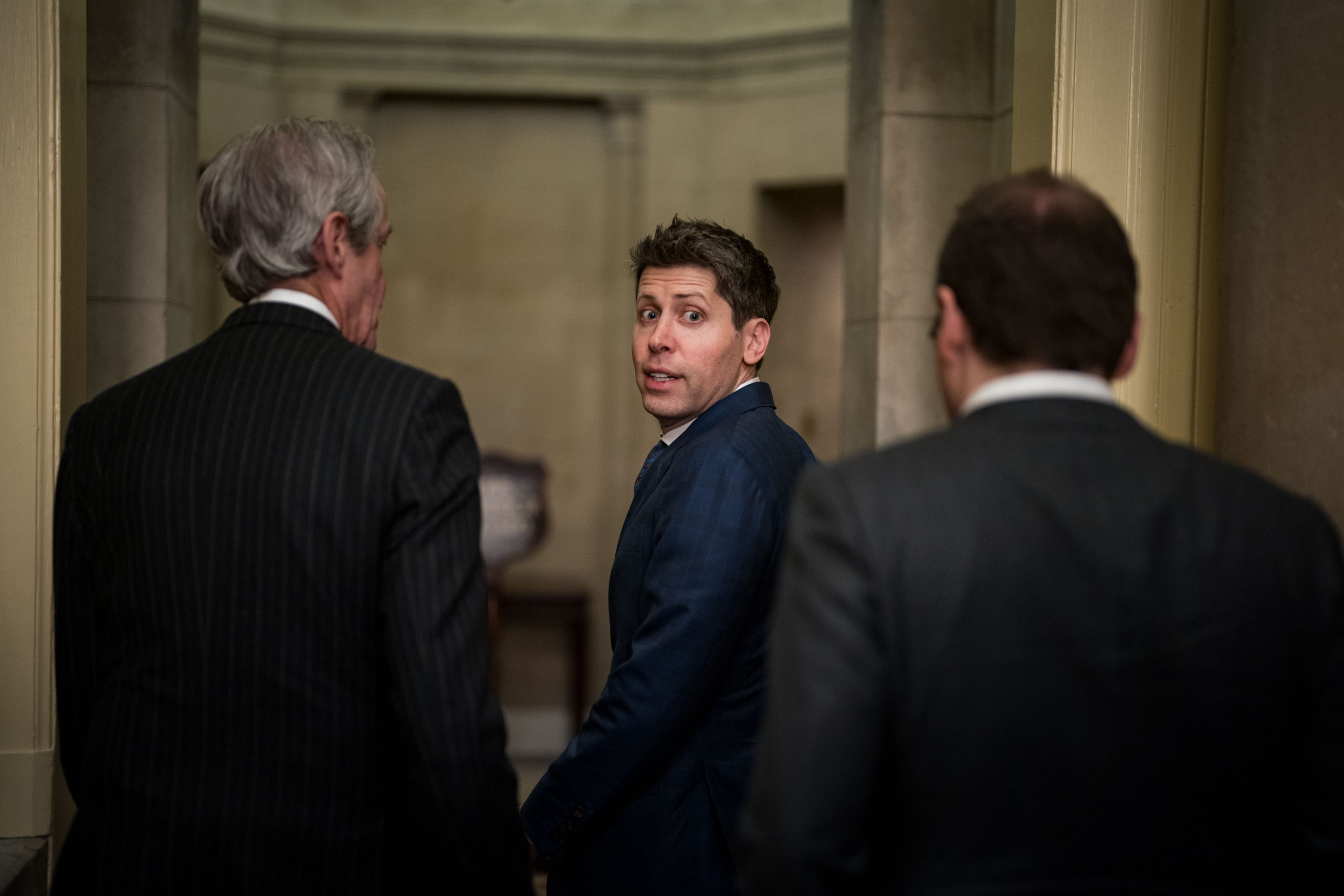Sam Altman looks behind him with a startled expression, walking through the U.S. Capitol building.