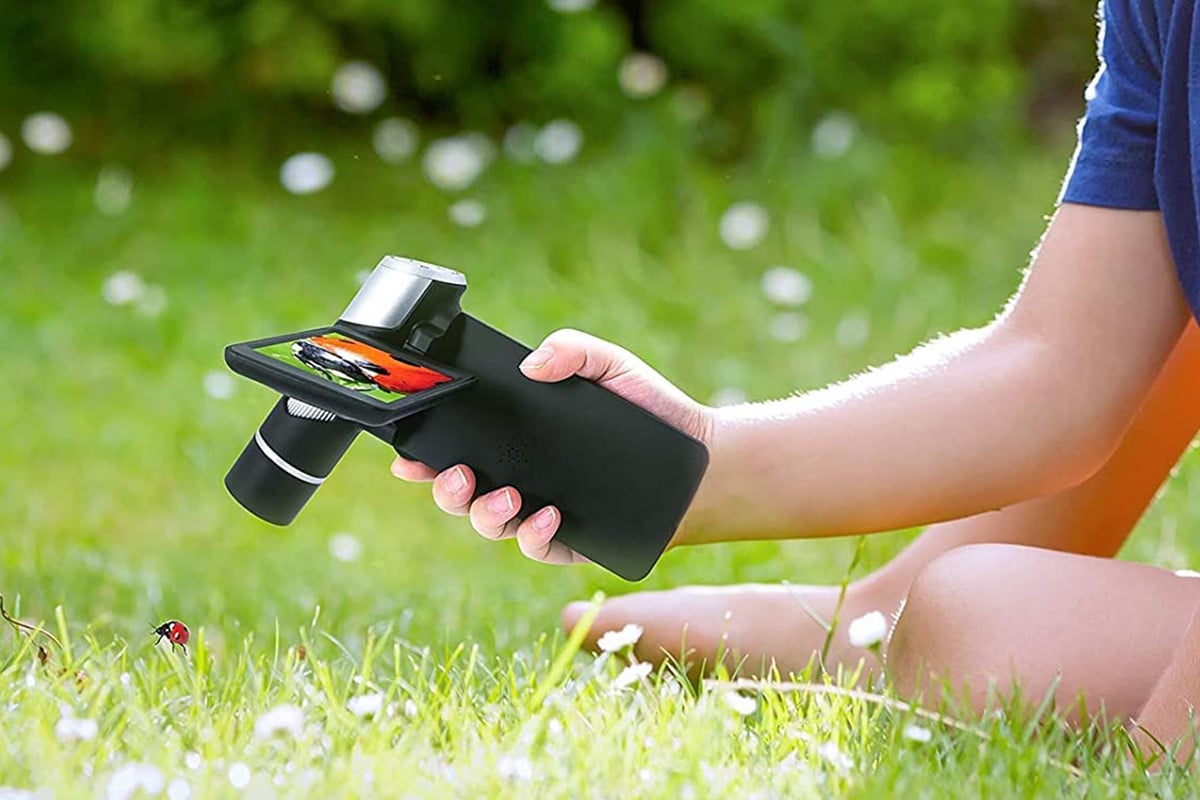 Man using handheld microscope to look at plants, insects.