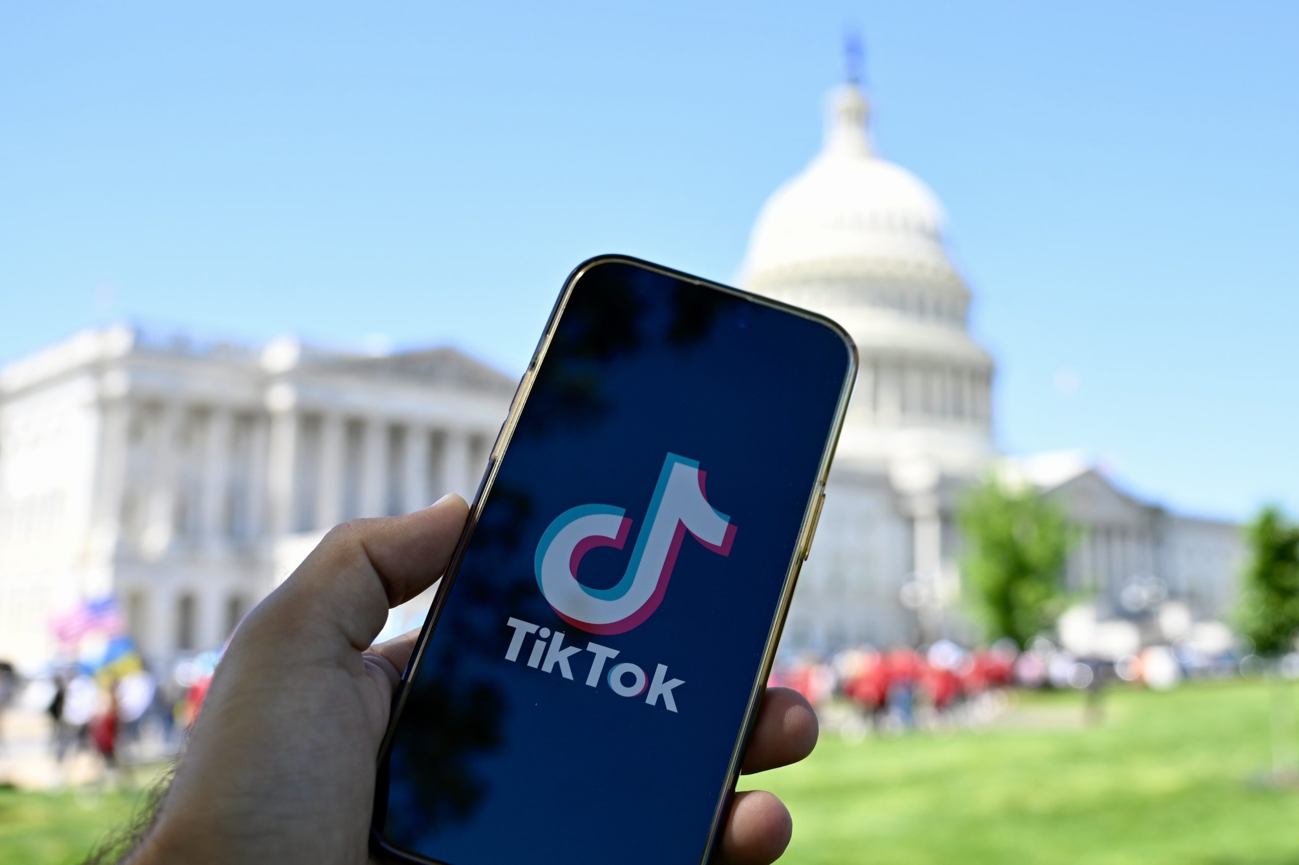 A phone displaying the TikTok logo in front of the White House. 