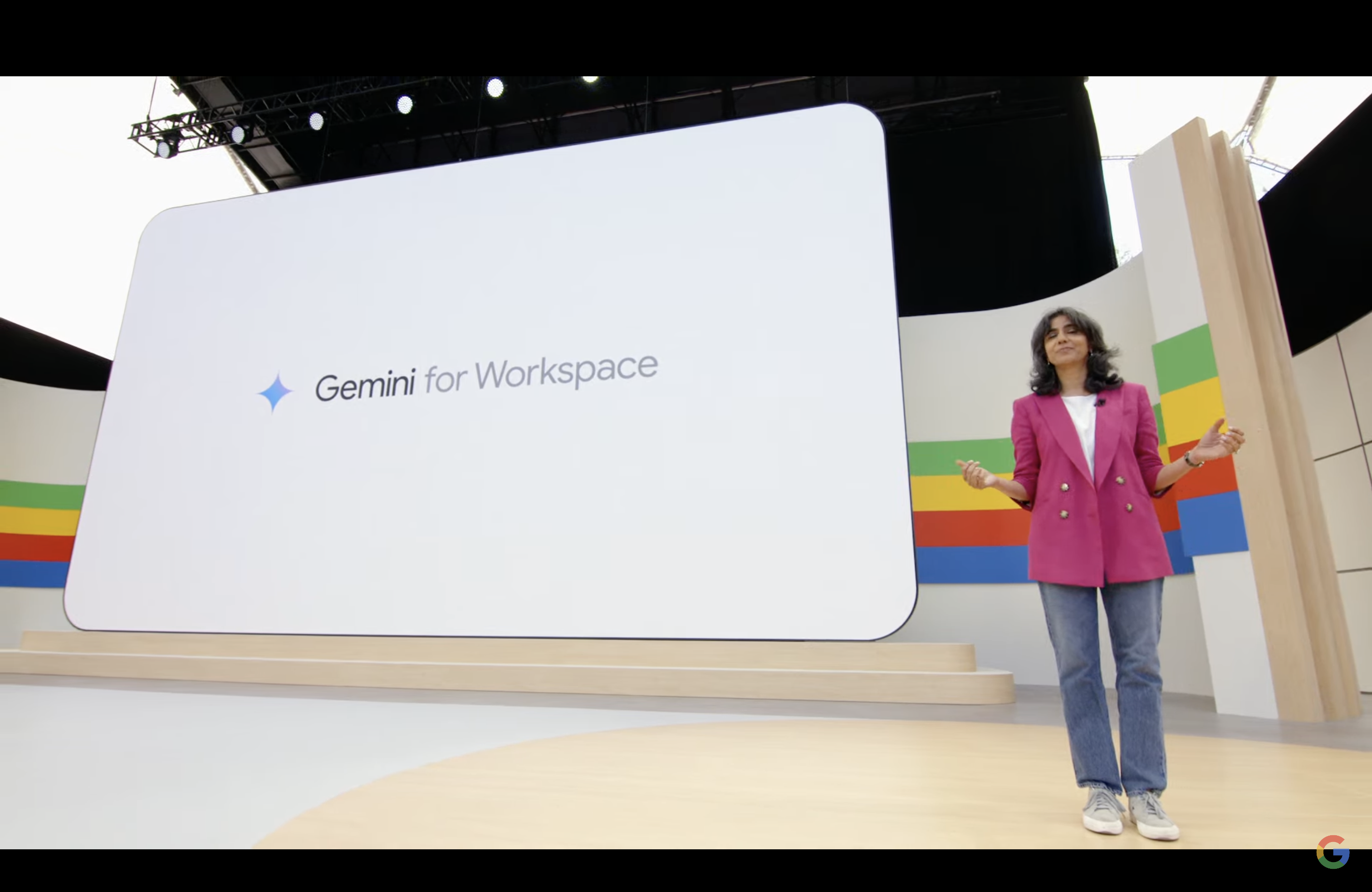 A woman on a stage in front of a screen with the words Gemini for Workspace