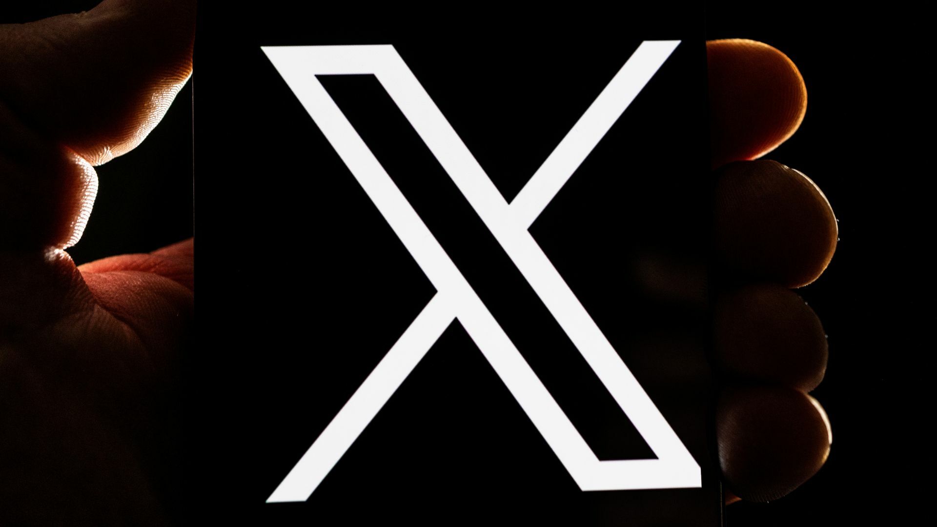 Hands holding a phone with the 'X' logo.