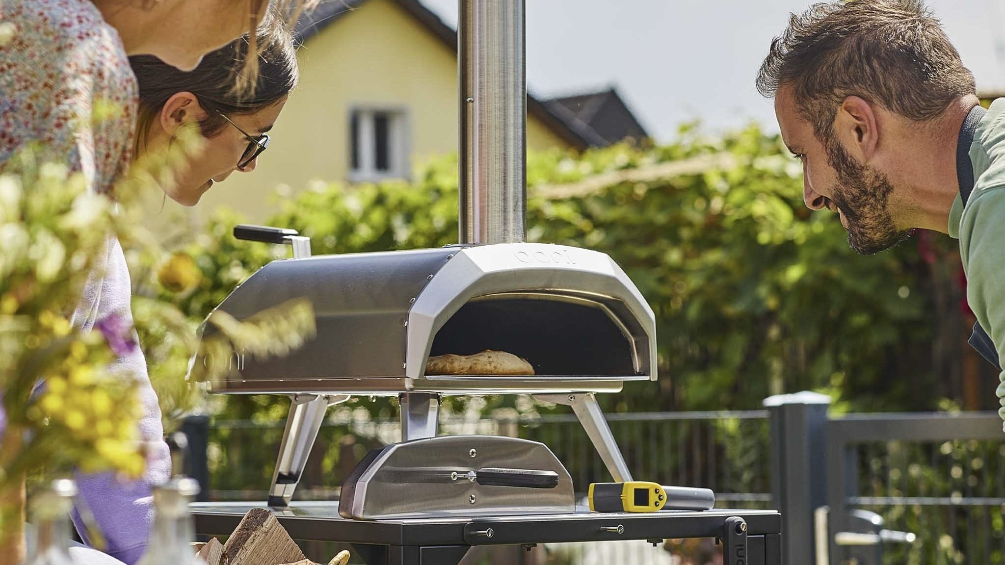 dad and family look at ooni pizza oven cooking pizza in their backyard