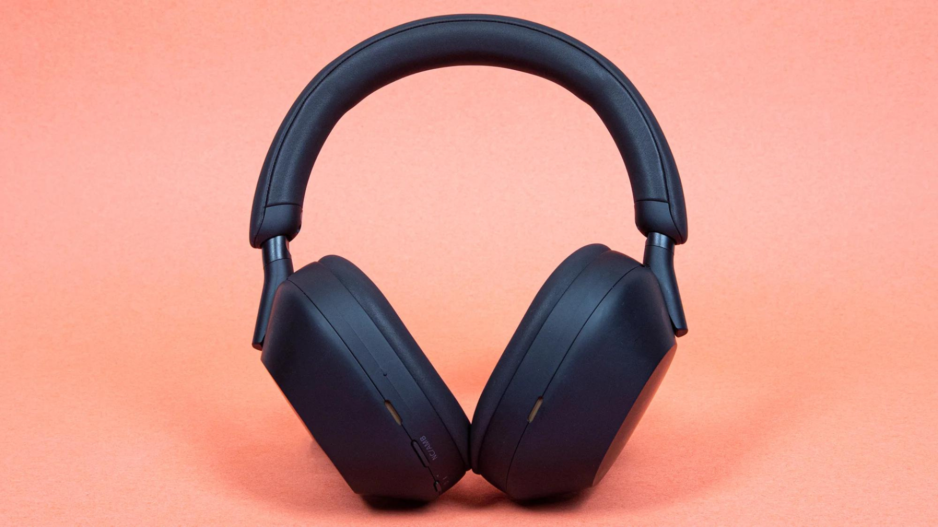 A pair of Sony WH-1000XM5 headphones against an orange background