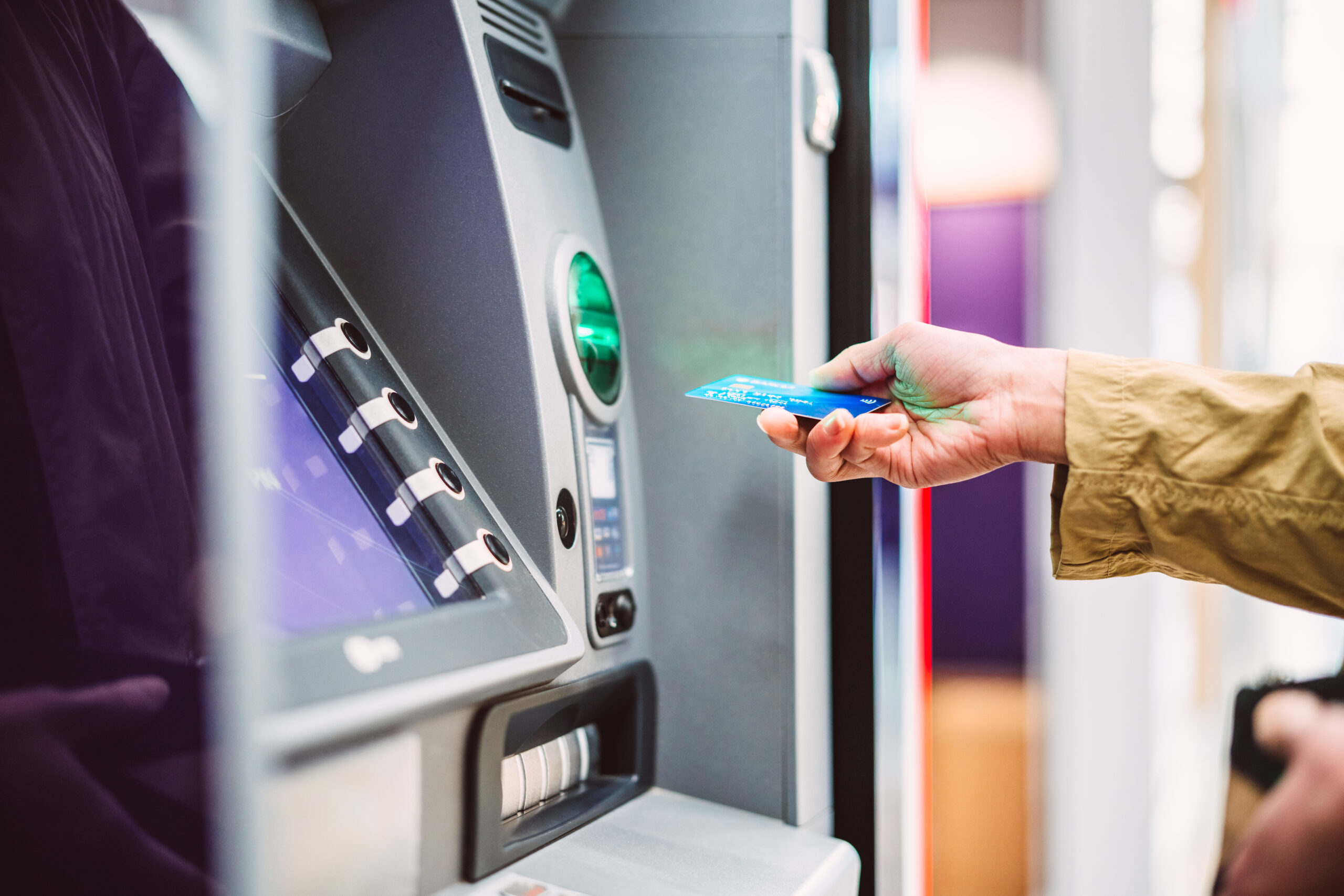 Female hand inserting bank card into automatic cash machine (ATM) to access bank account services in the city. Cash withdrawing, paying bills, checking account balance, transferring money, currency exchange at ATM. Self-service concept.