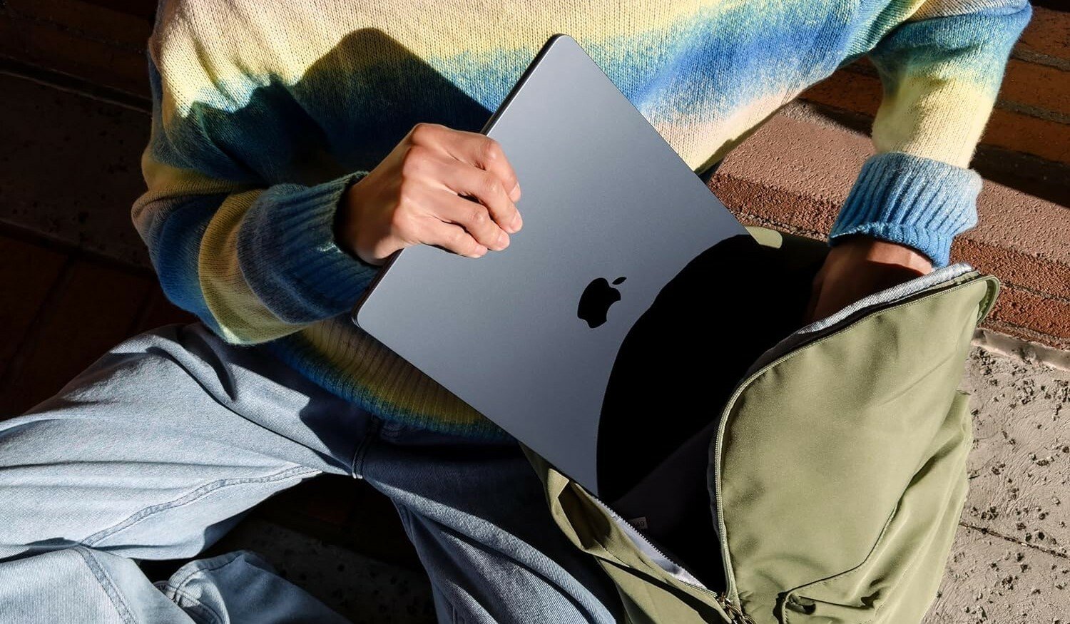 a person puts a black apple laptop into a green backpack