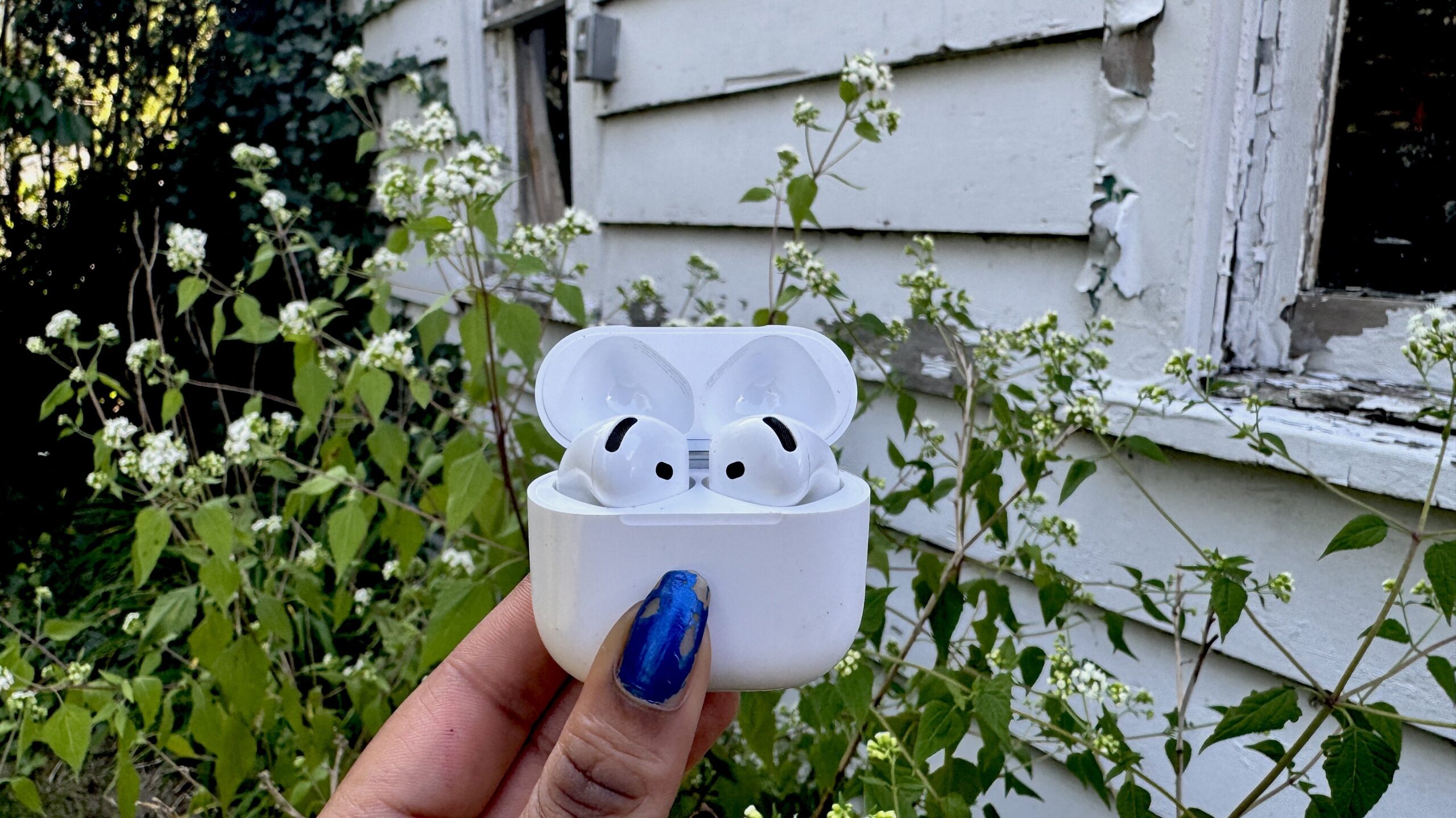 AirPods 4 in front of a tattered white shed