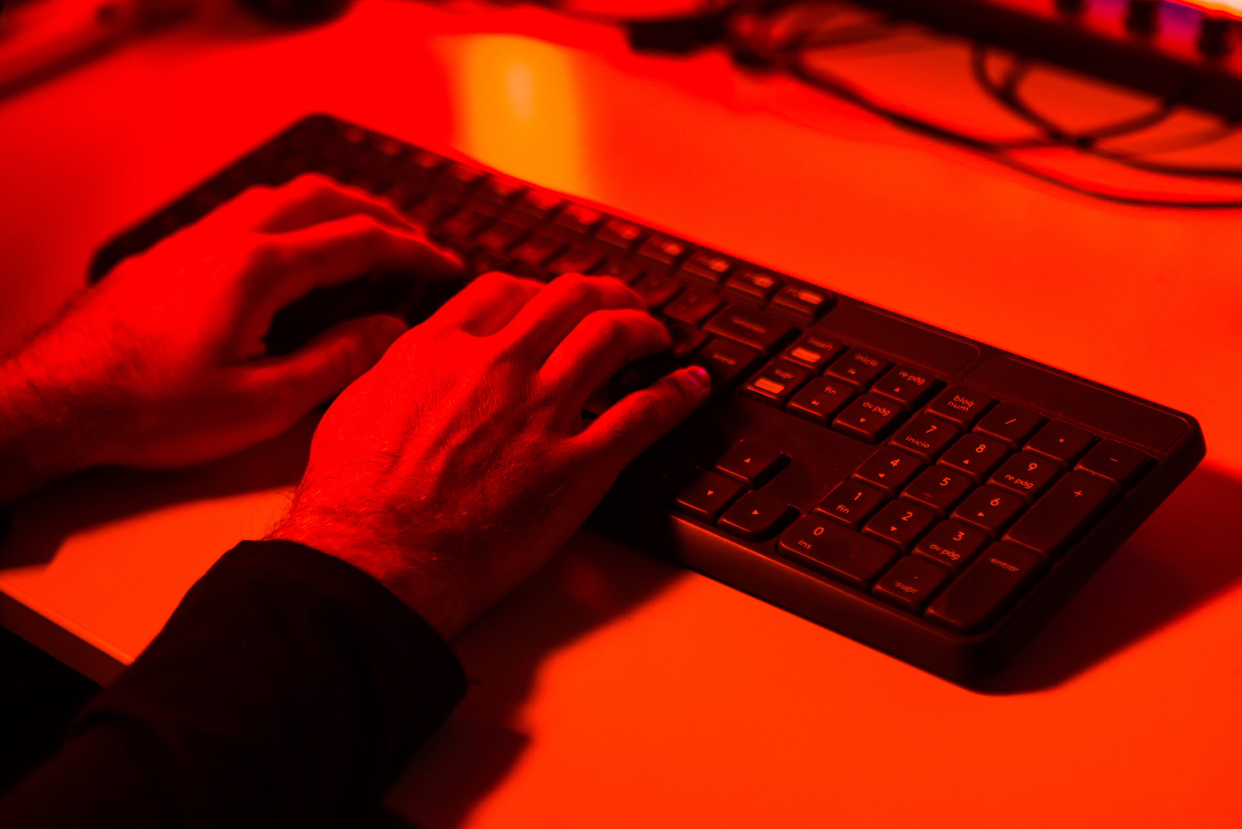 A hand typing on a keyboard bathed in red light. 