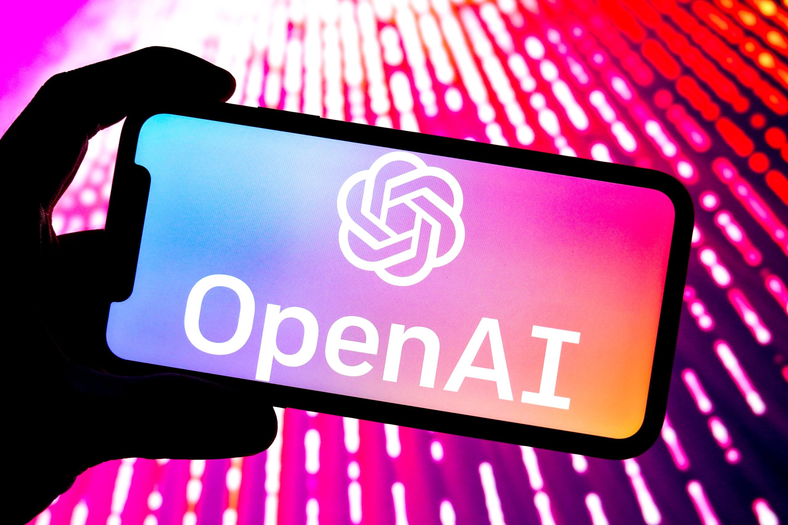 OpenAI logo open on a phone bathed in pink light. 