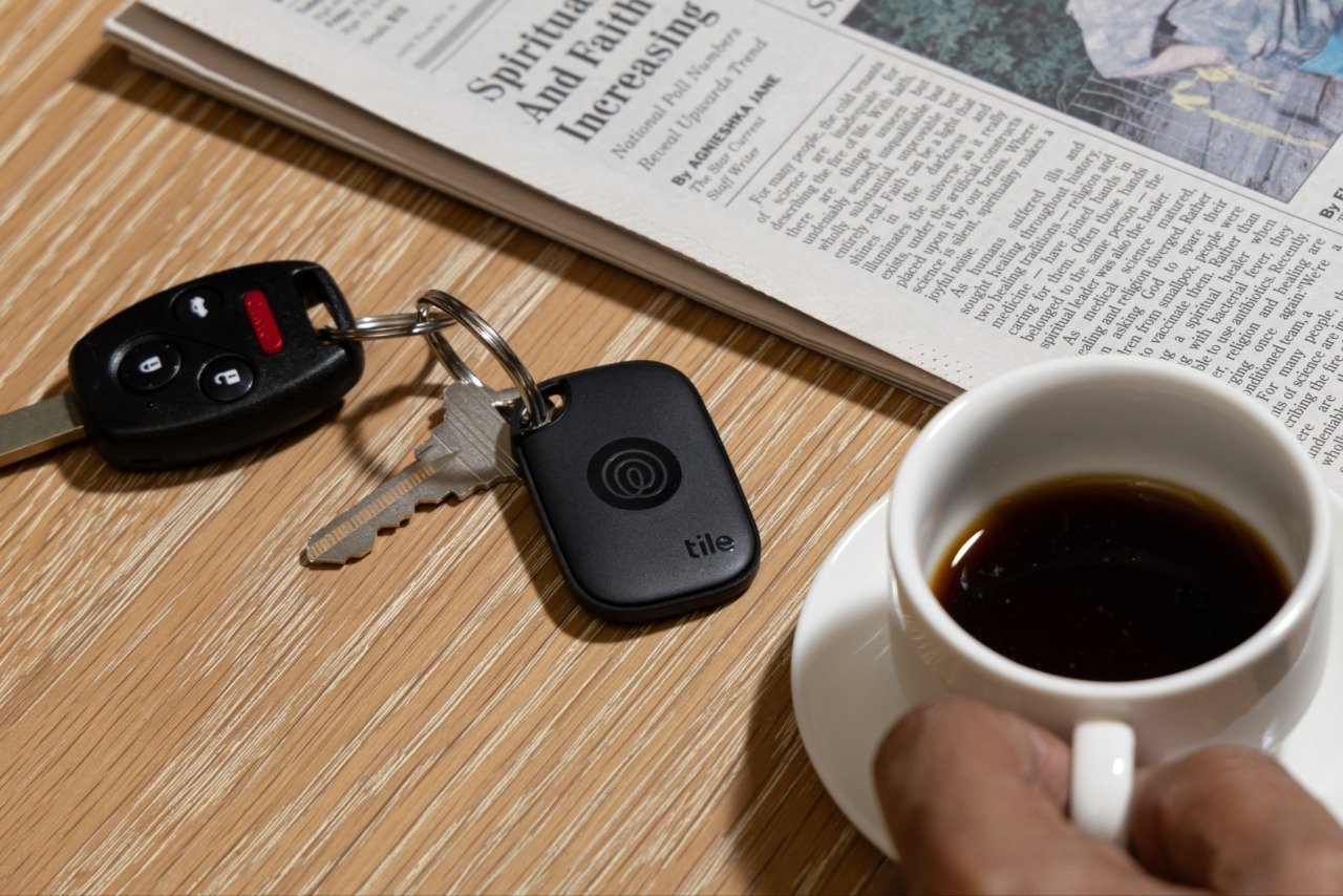 a tile tracker is attached to a keyring that sits on a tabletop next to a cup of coffee