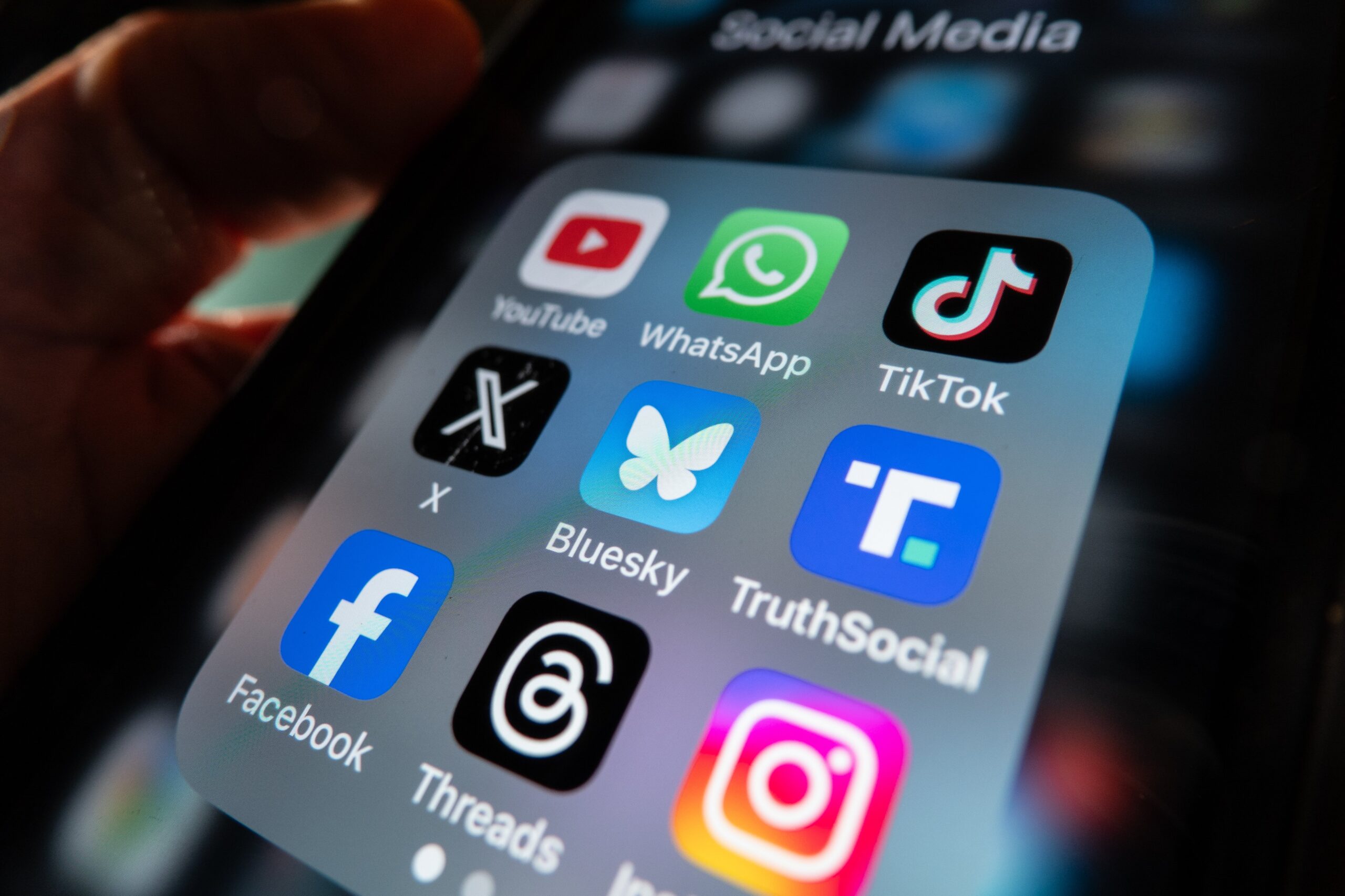 An iPhone app folder with several icons for popular social media apps, including Bluesky, X, and Truth Social.