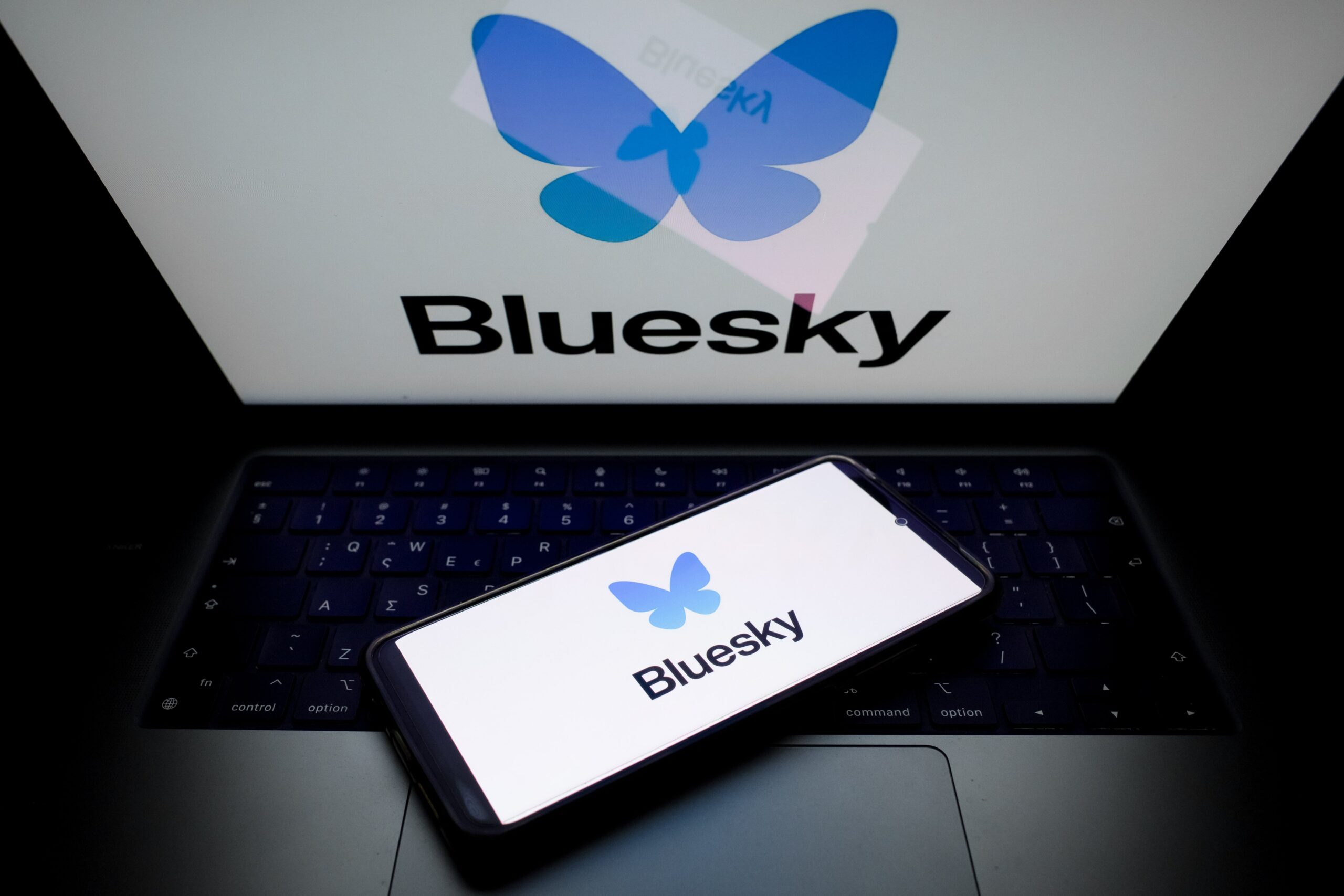 A glowing laptop screen and phone screen both display the Bluesky logo.