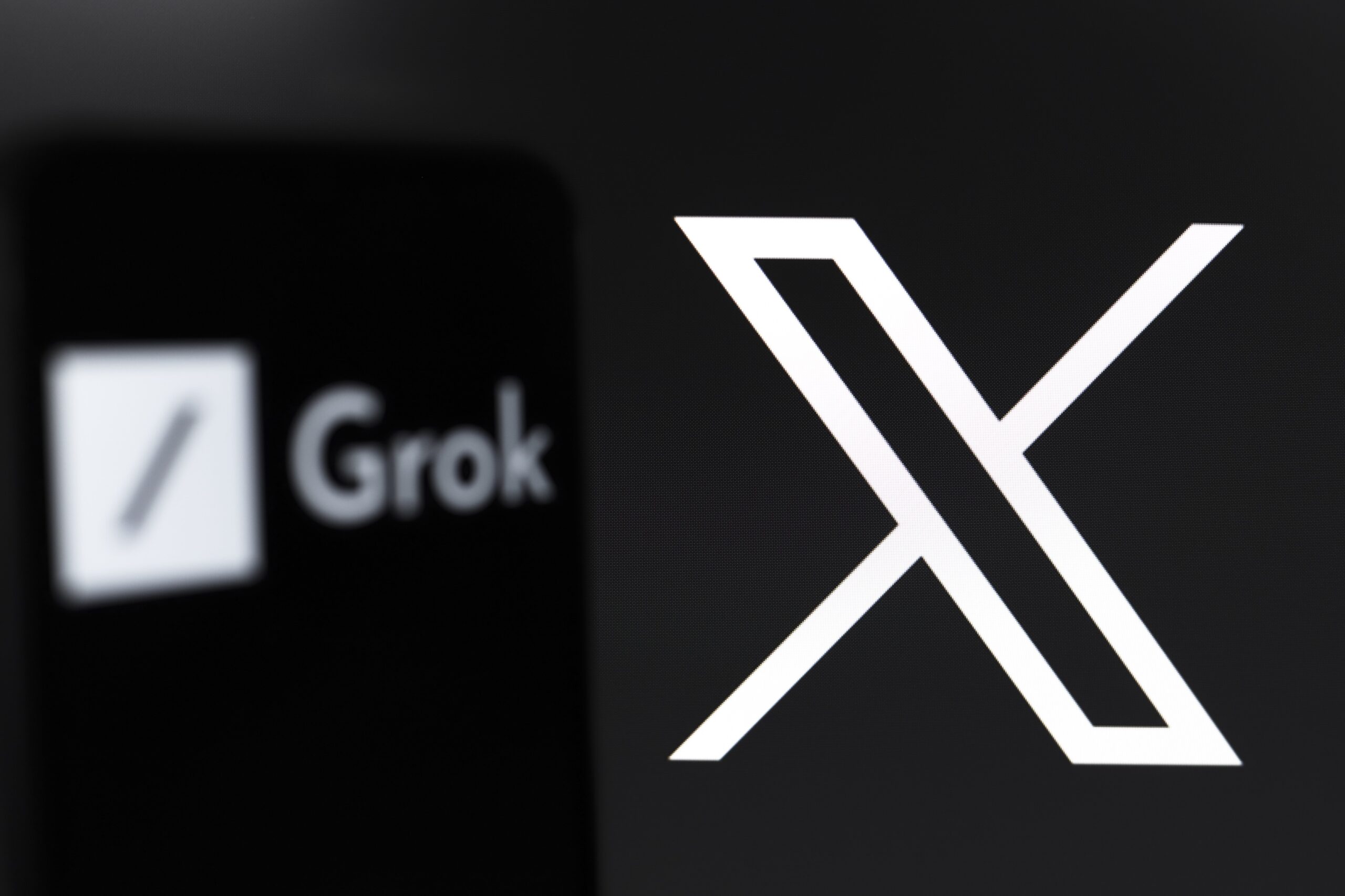 The Grok logo appears on the screen of a smartphone, and in the background, the logo of the social network X (formerly Twitter) is on the computer screen, in Reno, United States, on November 12, 2024. Grok is an artificial intelligence chatbot generative technology developed by xAI, with an initiative from Elon Musk. The company tests a free version of the service that will be available soon.